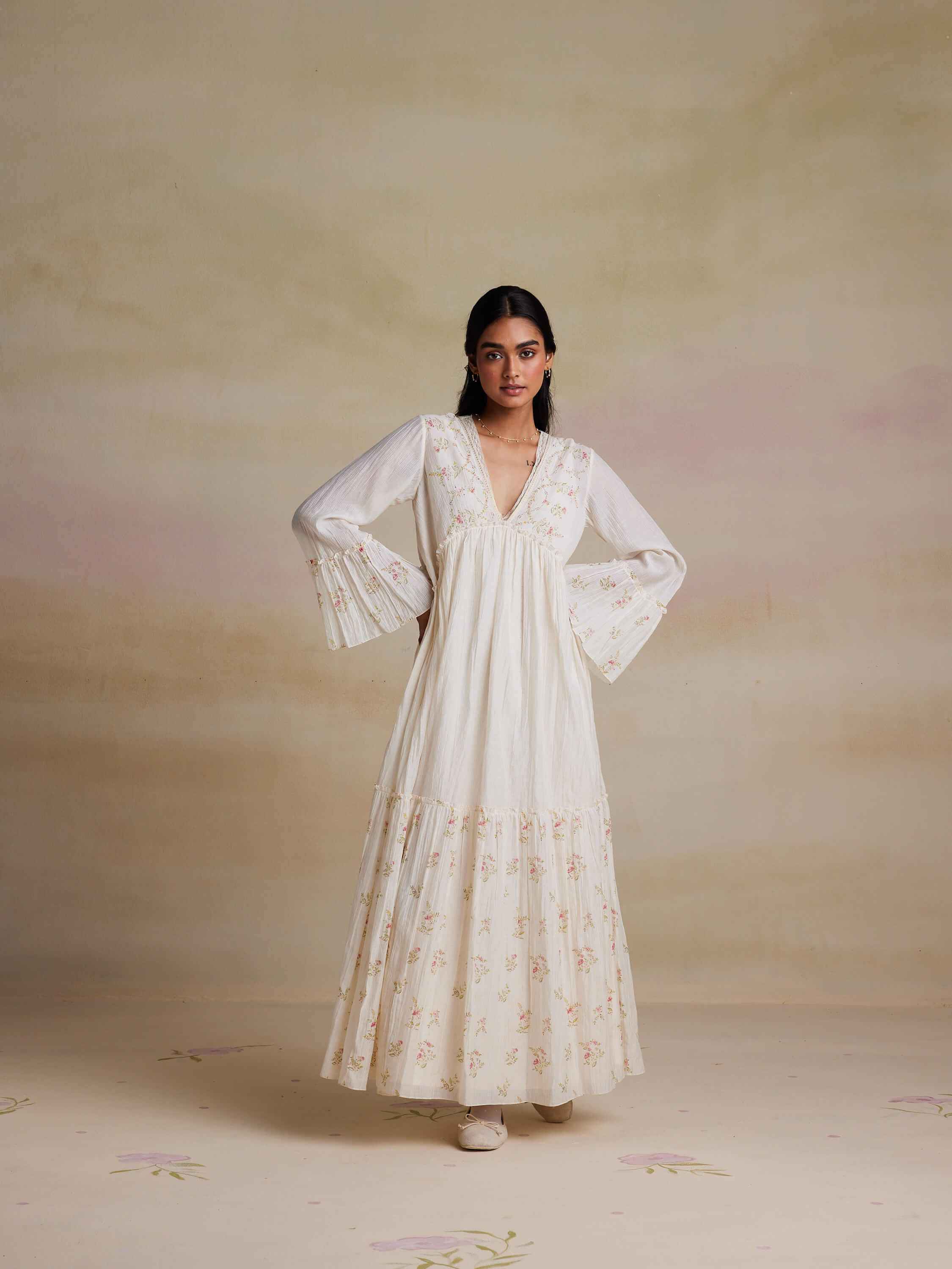 Woman wearing a long, white, floral dress with bell sleeves.