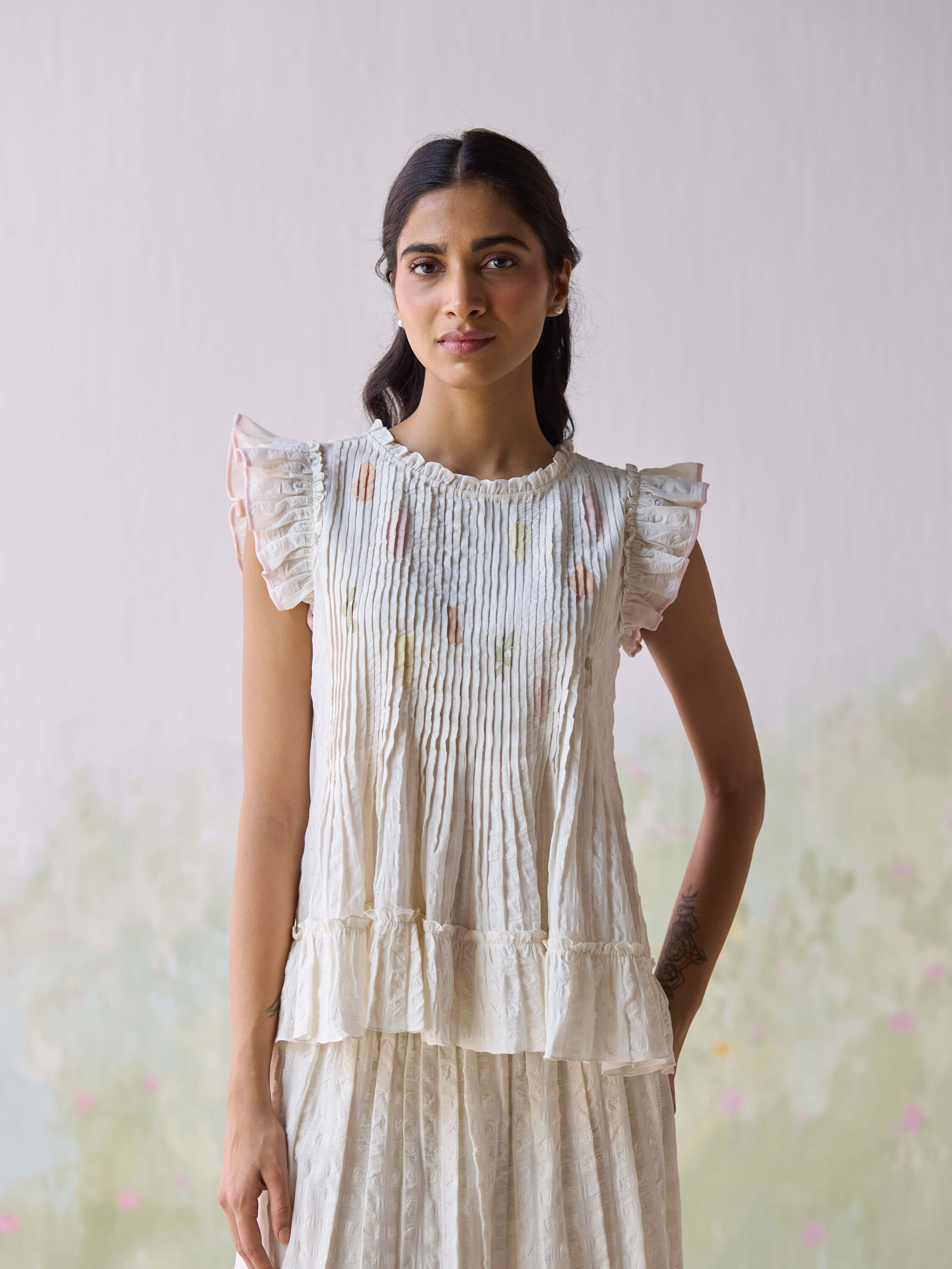 Woman wearing a cream-colored ruffled sleeveless blouse against a soft background