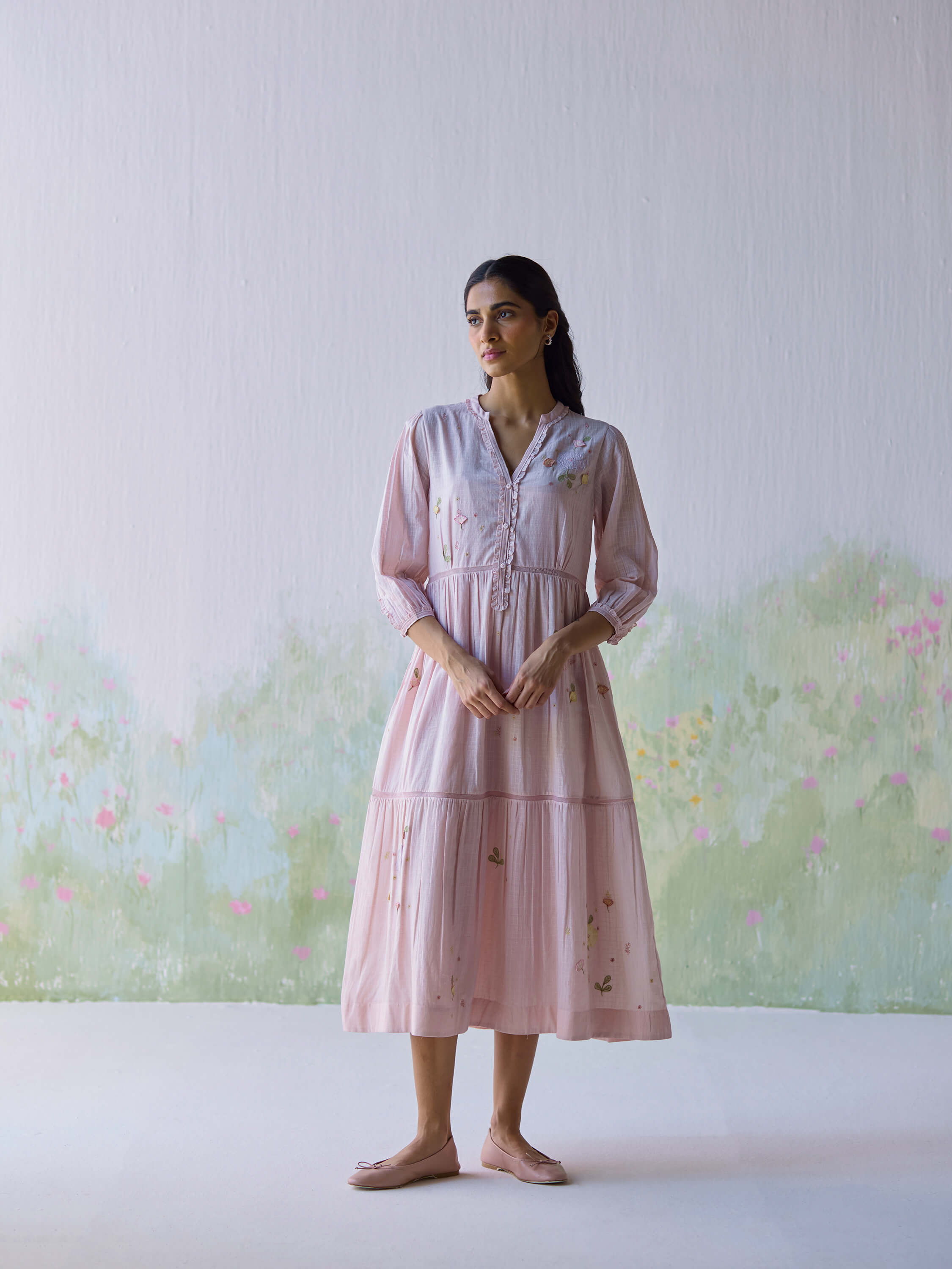 Woman in pink floral dress standing against a painted floral backdrop.