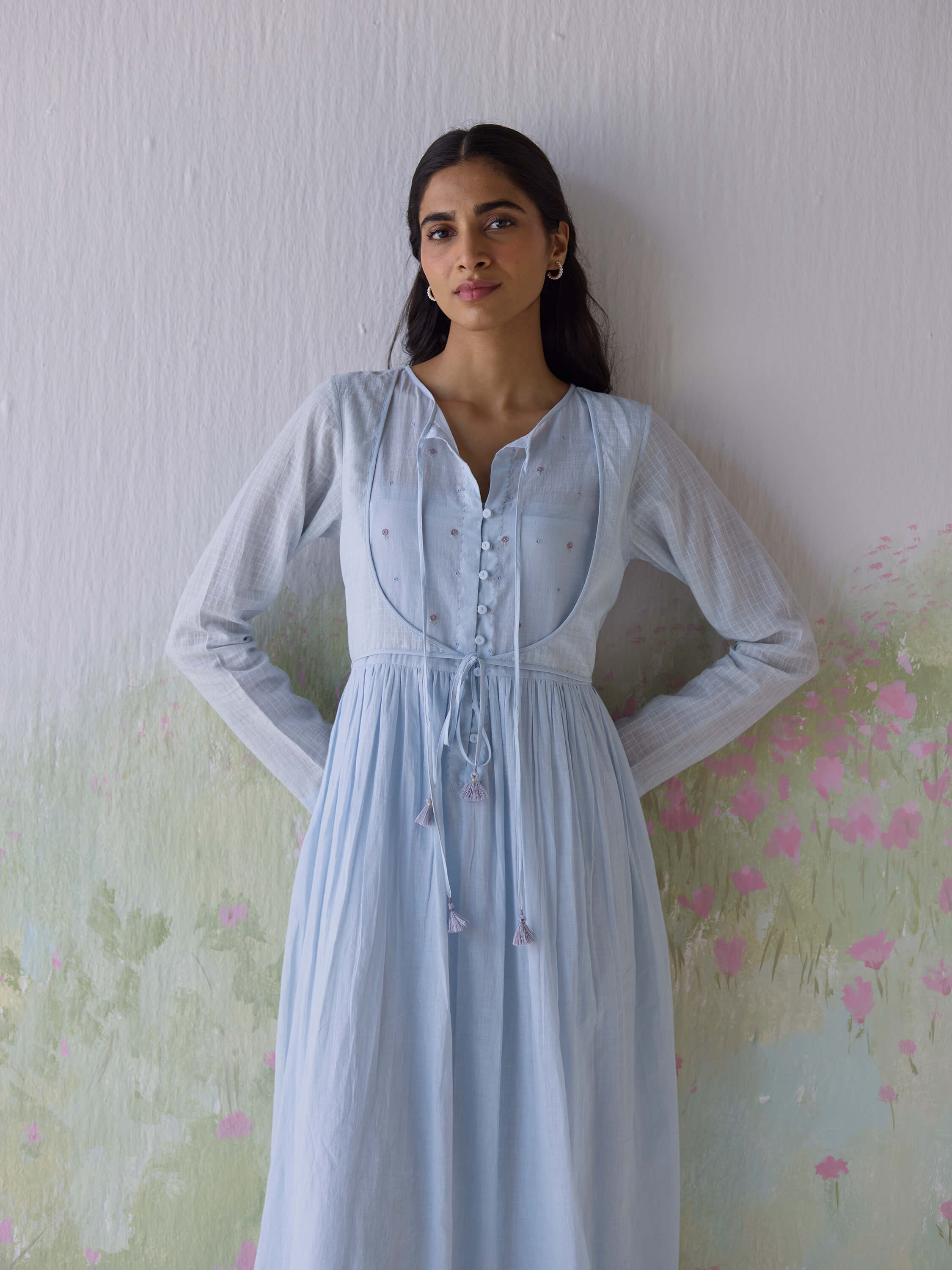 Woman in light blue dress standing against a floral wall.