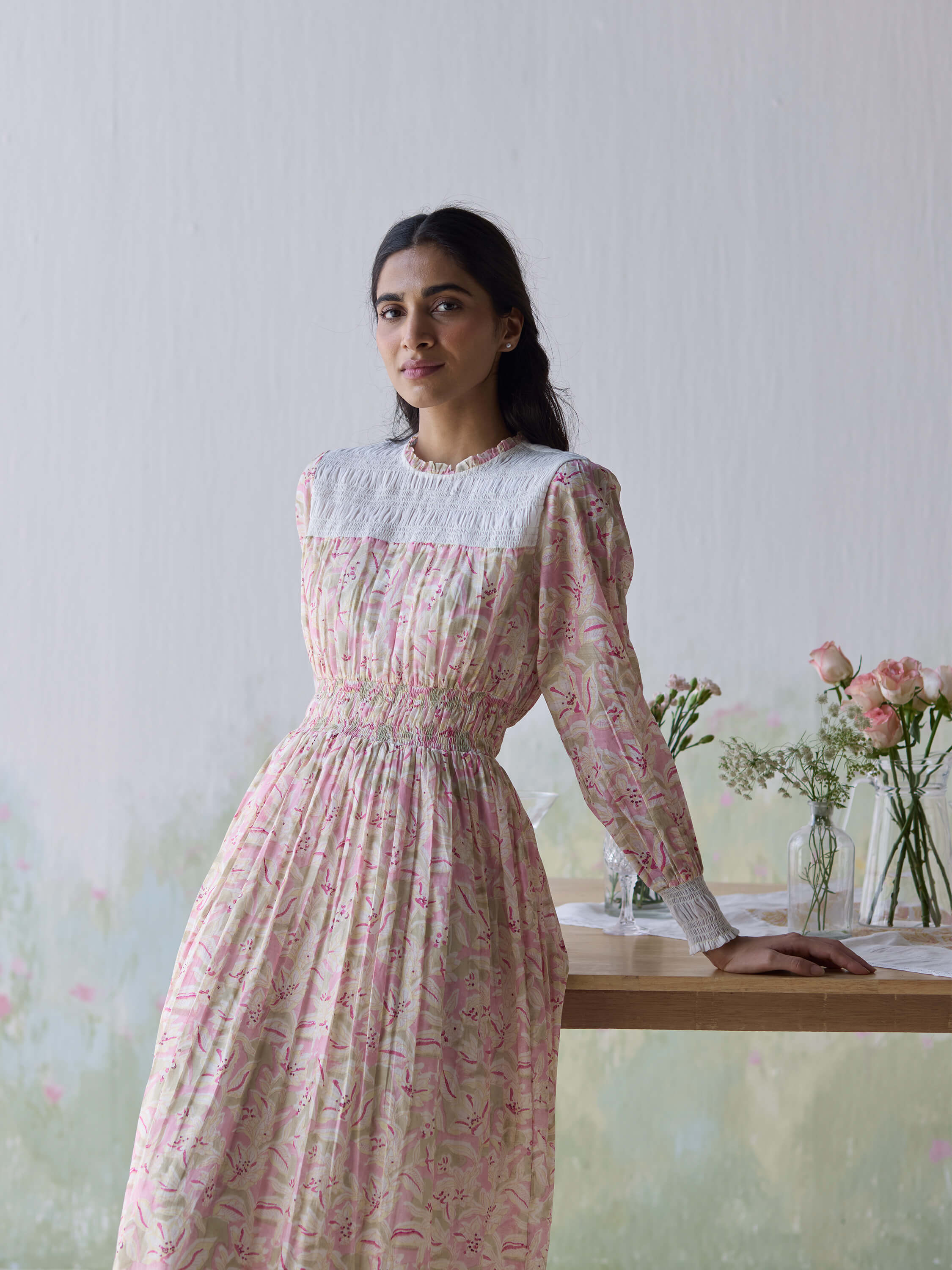 Woman in floral dress standing by a table with flowers.