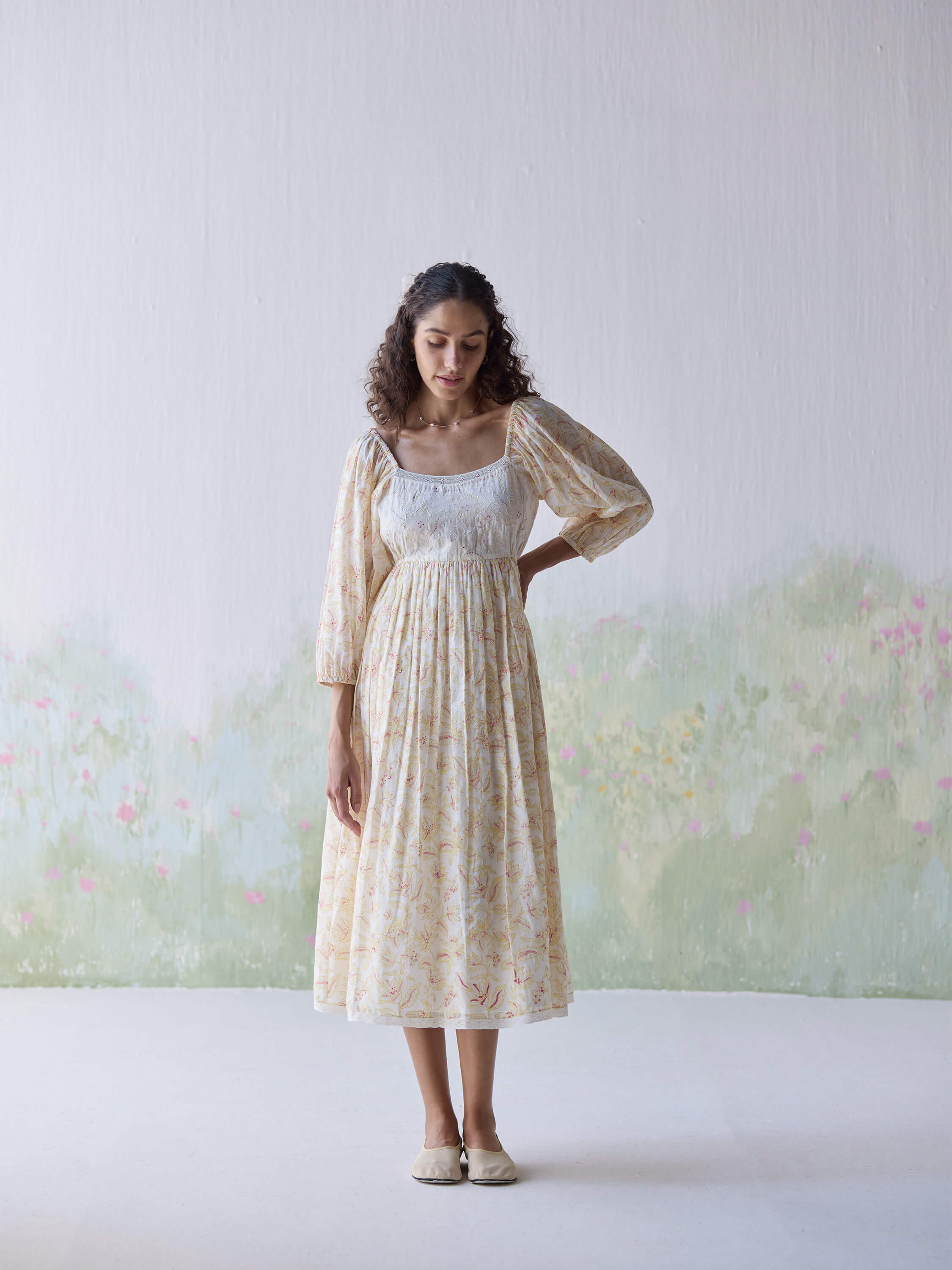 Woman in floral dress posing against a pastel floral wall
