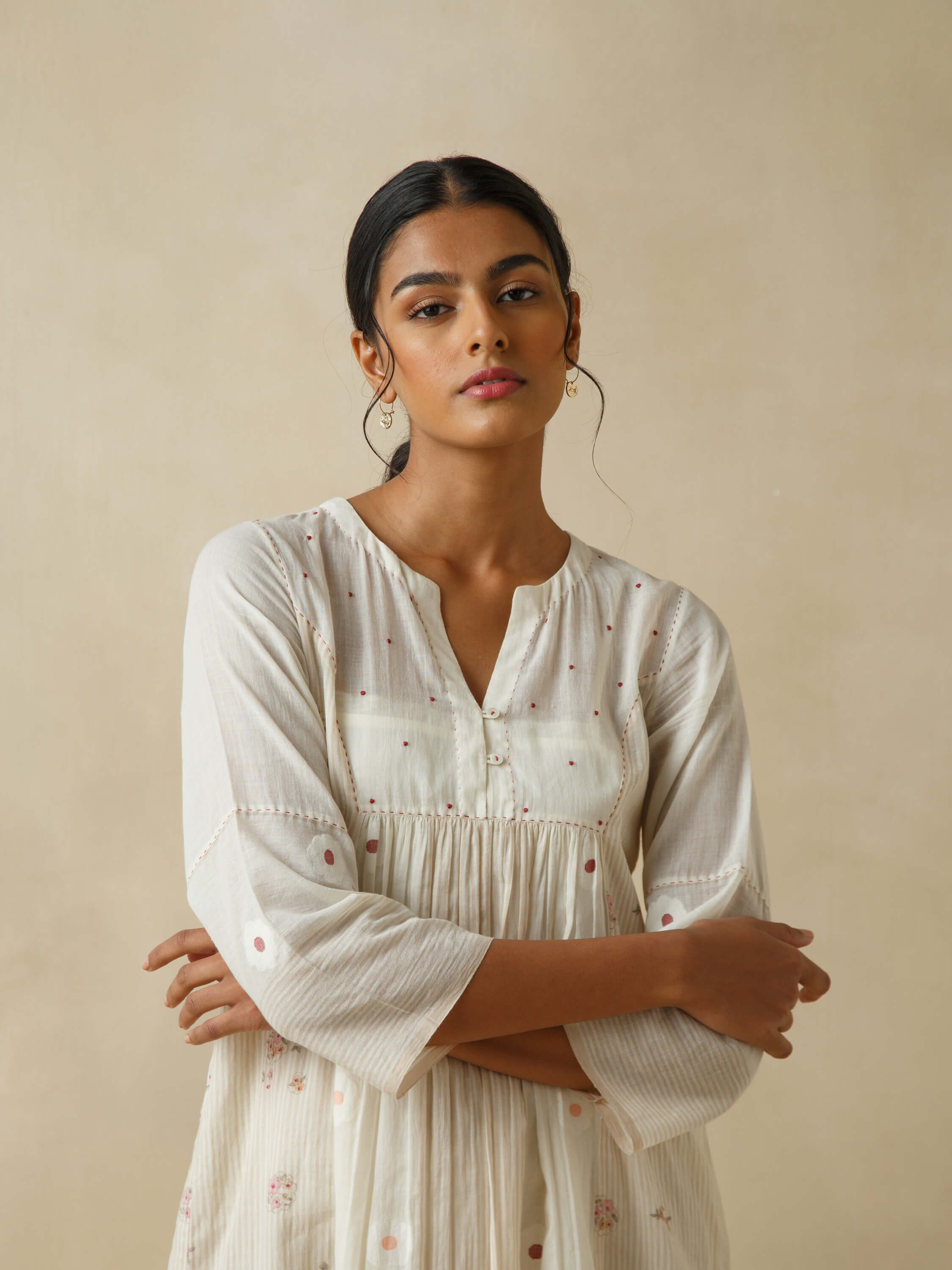 Woman in elegant, white embroidered dress with neutral background.