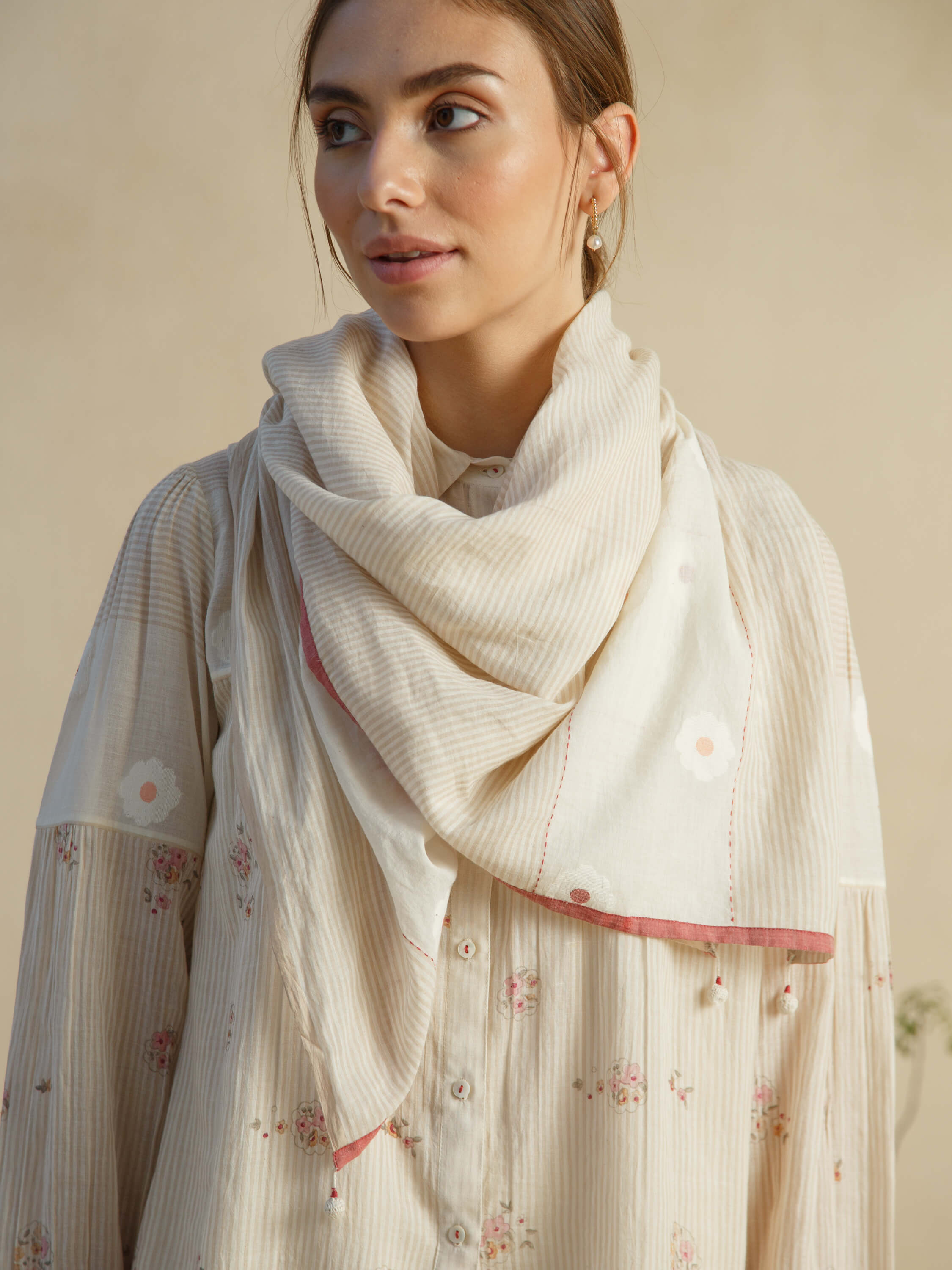 Woman wearing a white floral blouse and light scarf indoors.