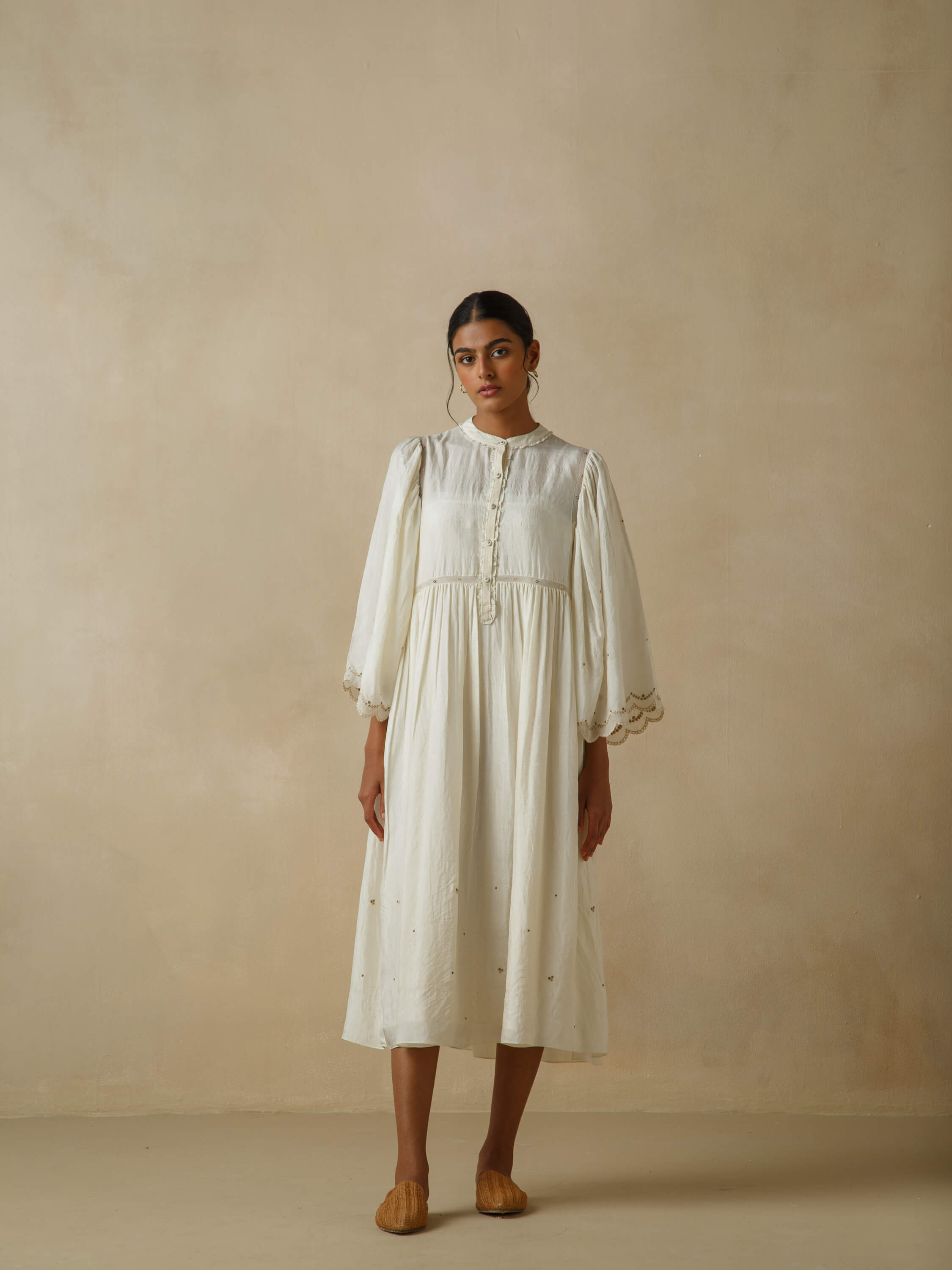 Woman in elegant white dress with embroidered details standing indoors.