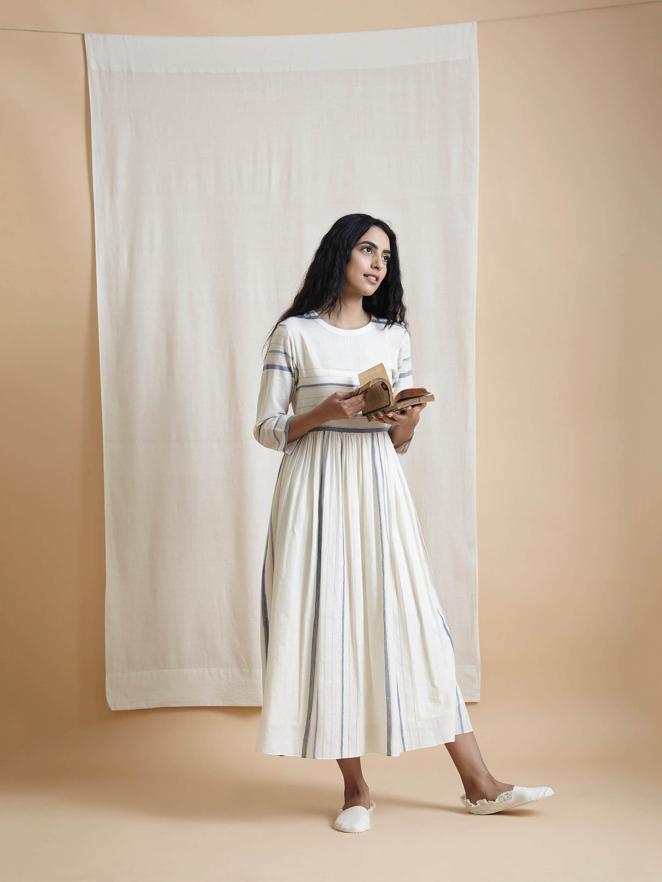 Woman dressed in white holding books in a minimalist setting.