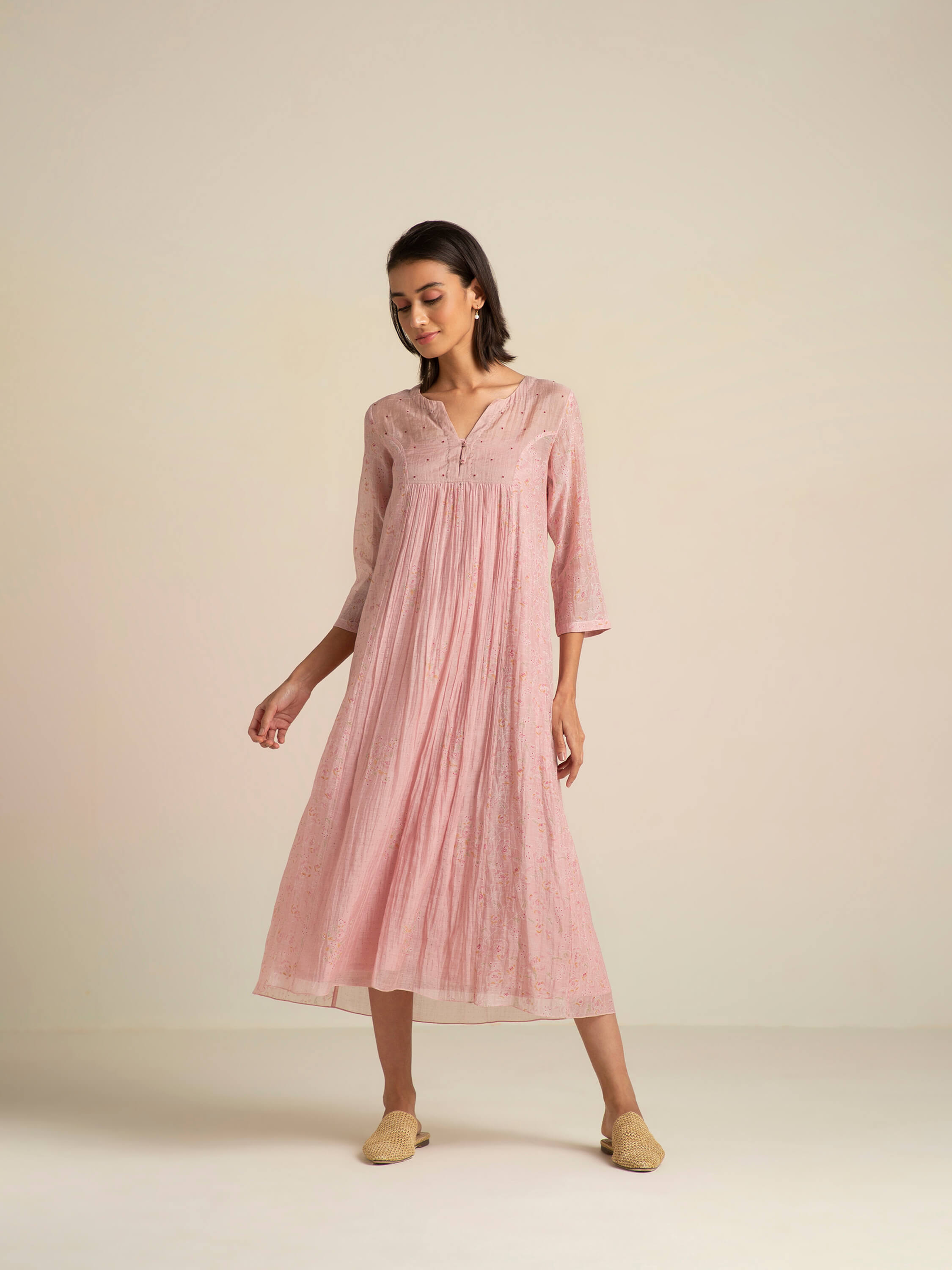 Woman wearing a pink flowy long dress and beige slippers.