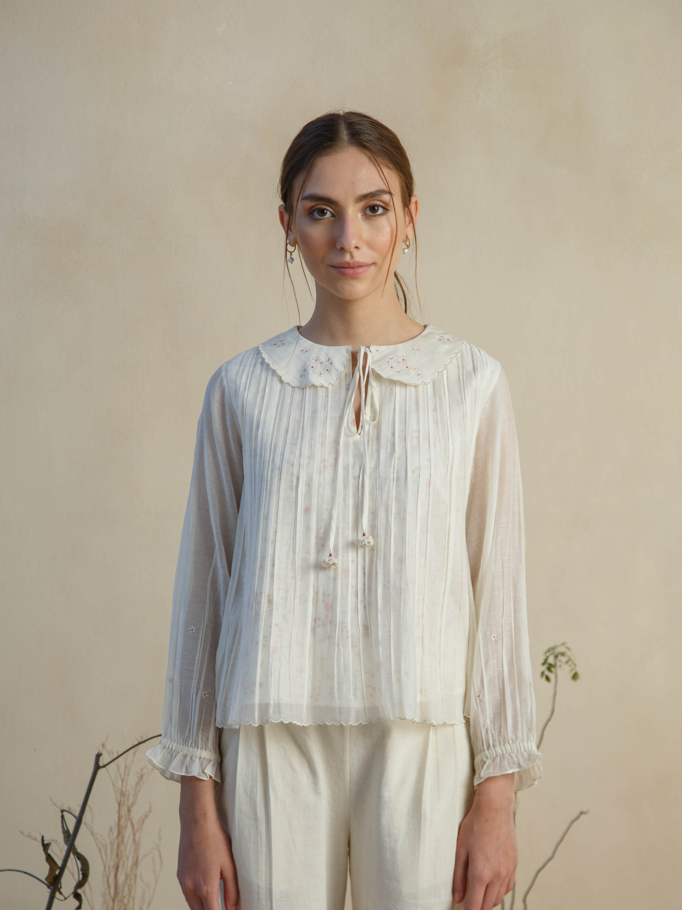 Woman wearing a white blouse with delicate embroidery details.