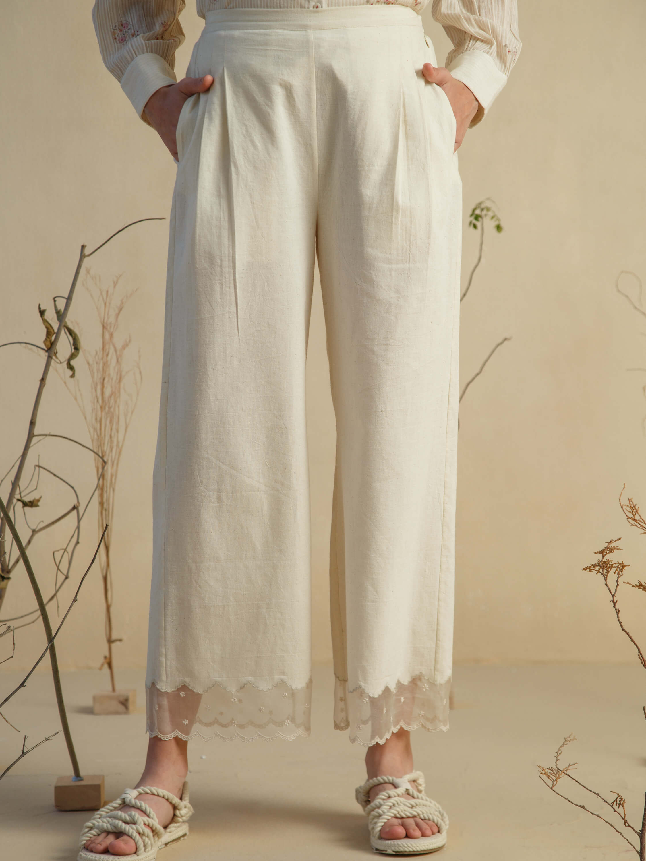 Woman wearing high-waisted white pants with lace trim details.