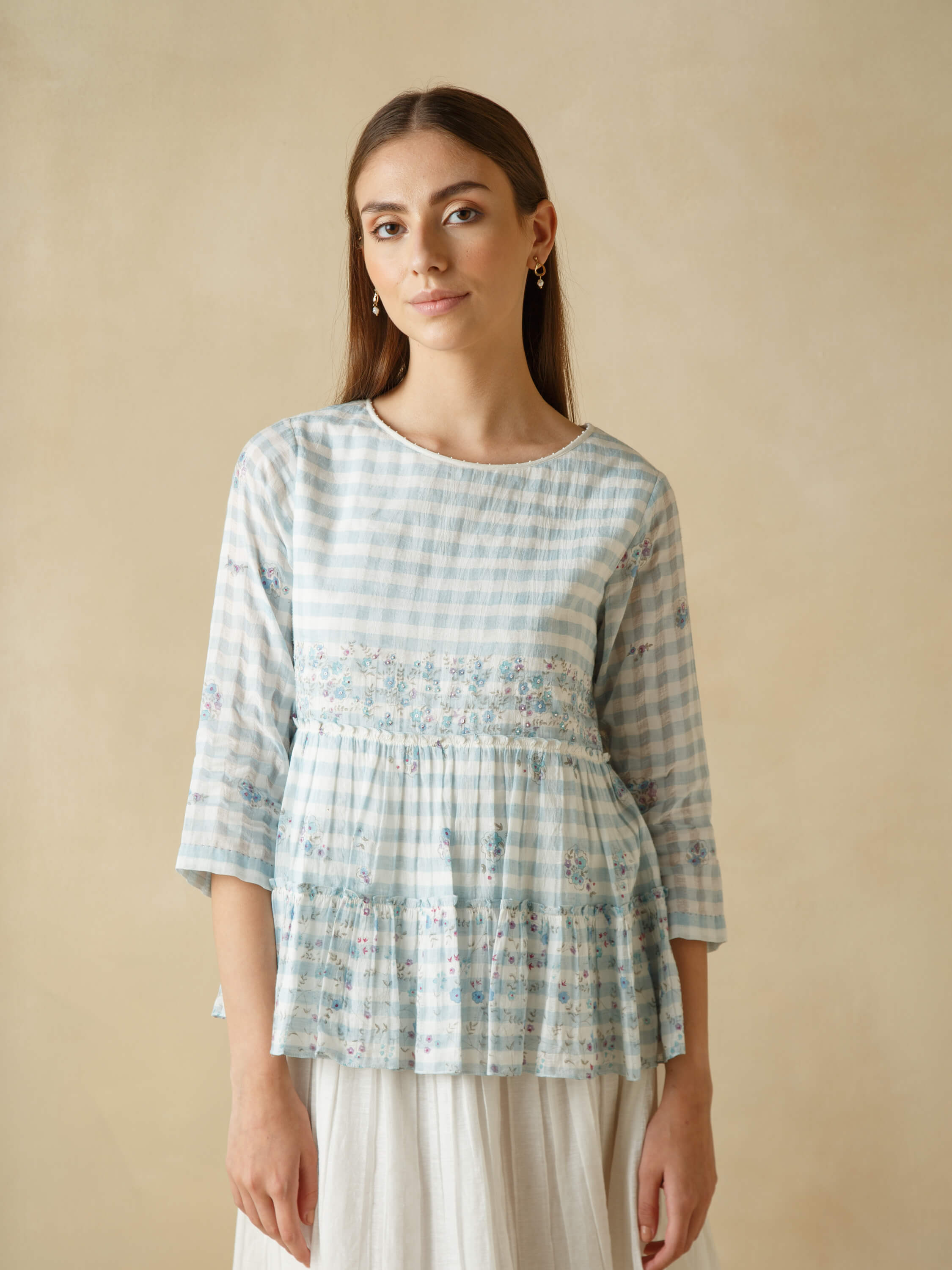 Woman wearing a light blue patterned blouse with a serene backdrop.