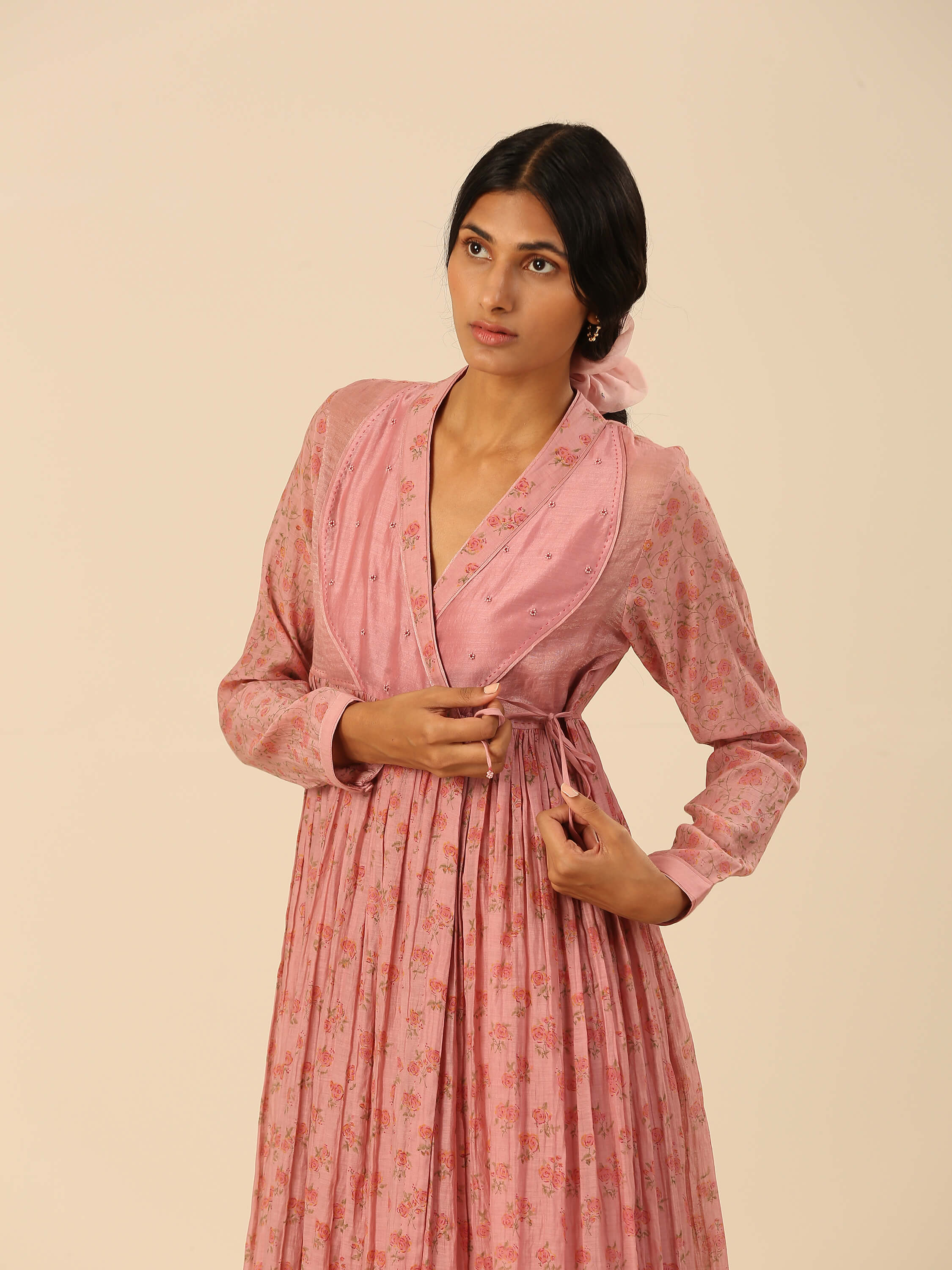 Woman wearing a pink floral dress adjusting waist tie.
