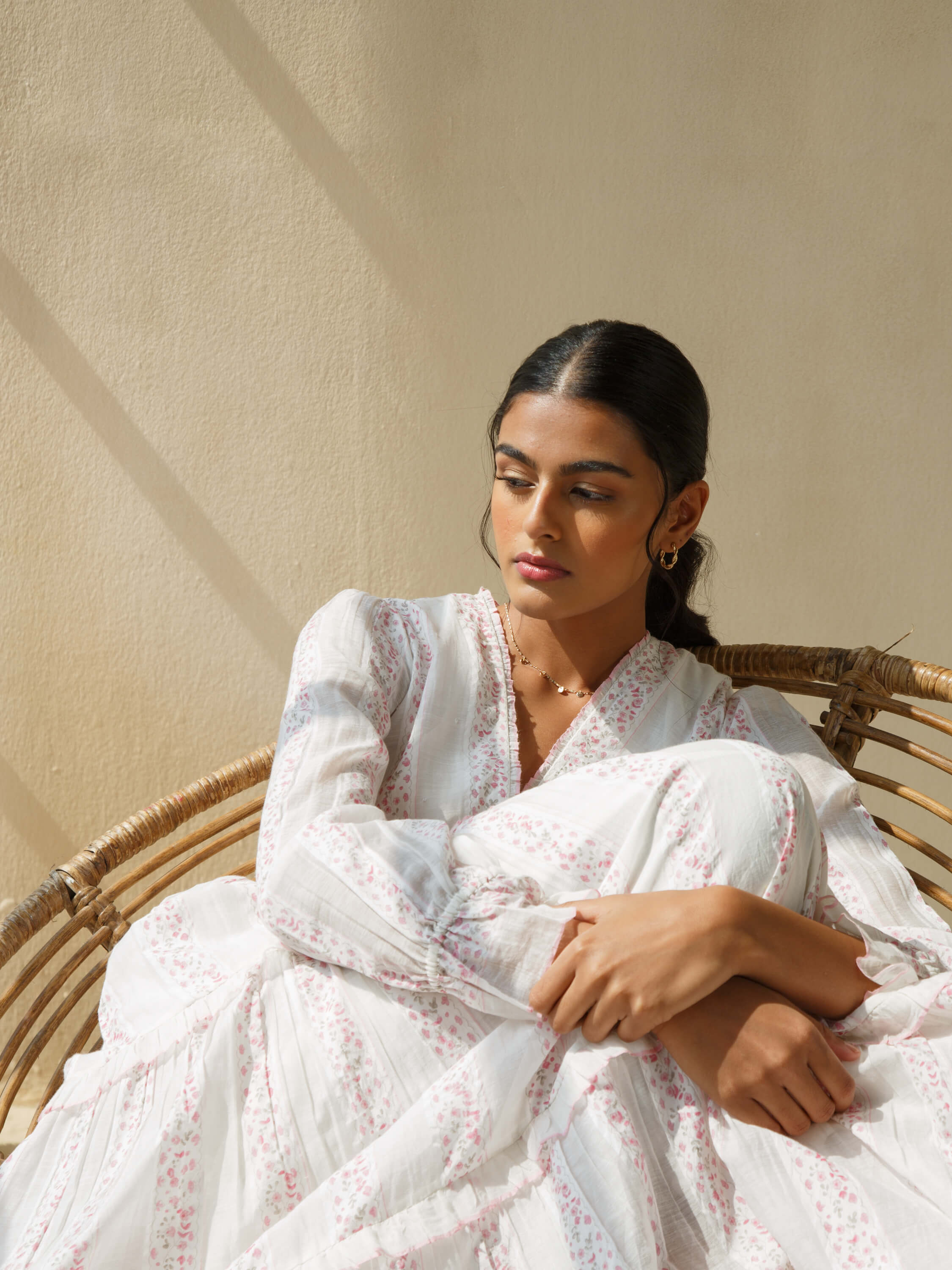 Woman in white floral dress sitting in wicker chair.