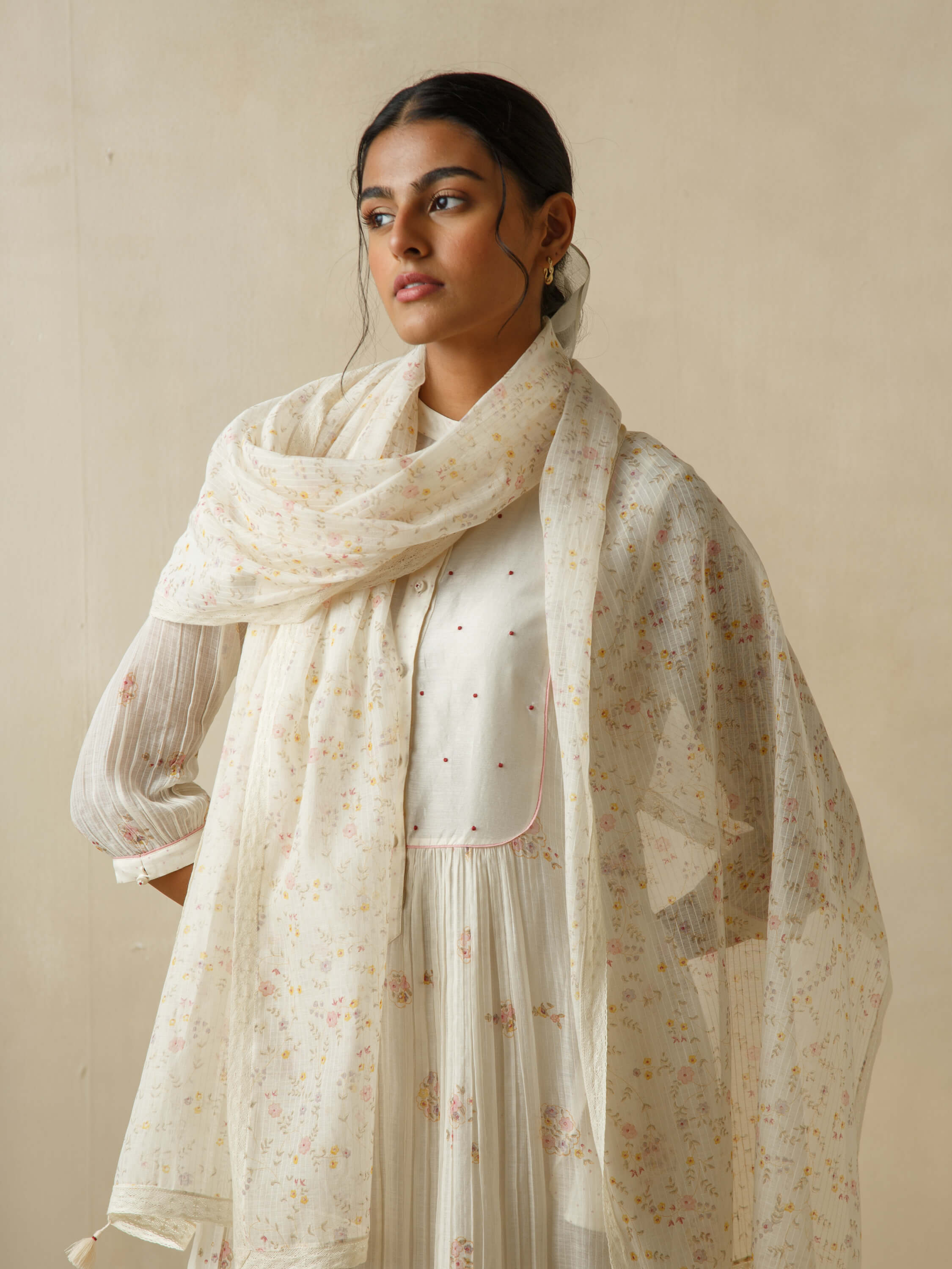 Woman in elegant traditional white floral dress set against neutral background.