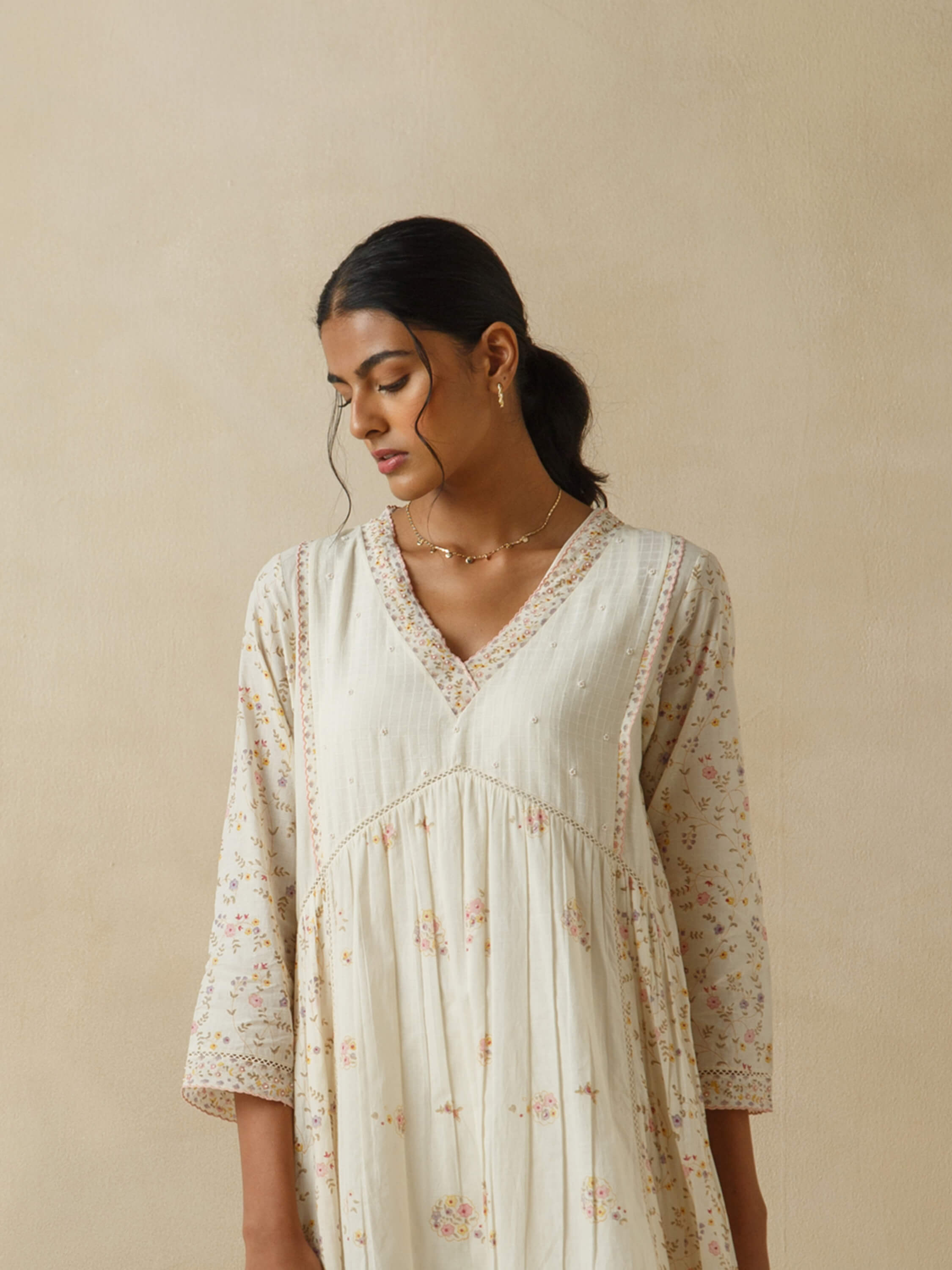 Woman in beige floral dress with neutral background.