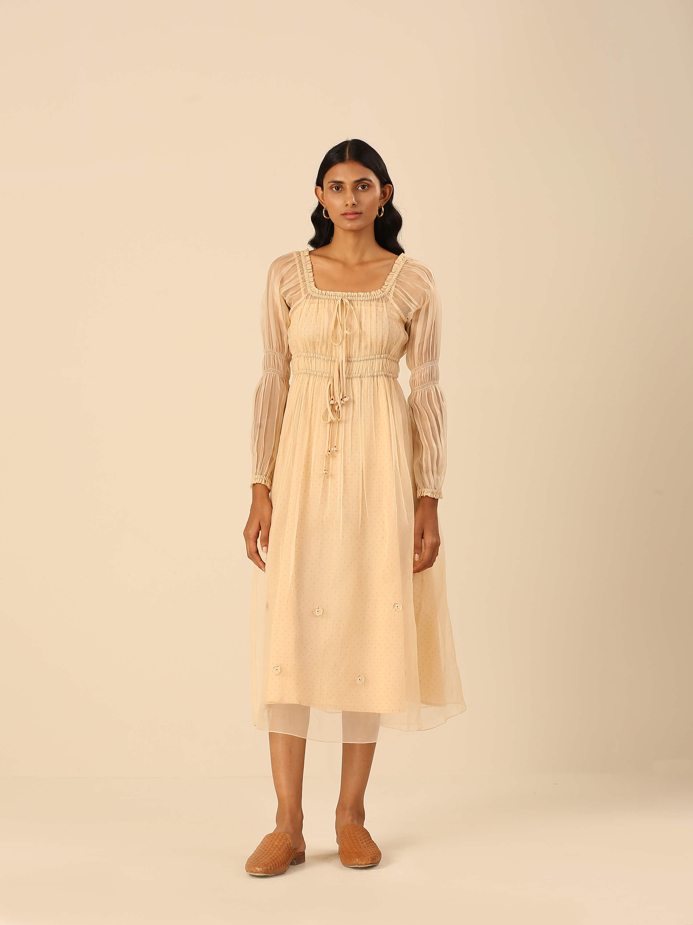 Woman wearing a beige midi dress with long sheer sleeves.