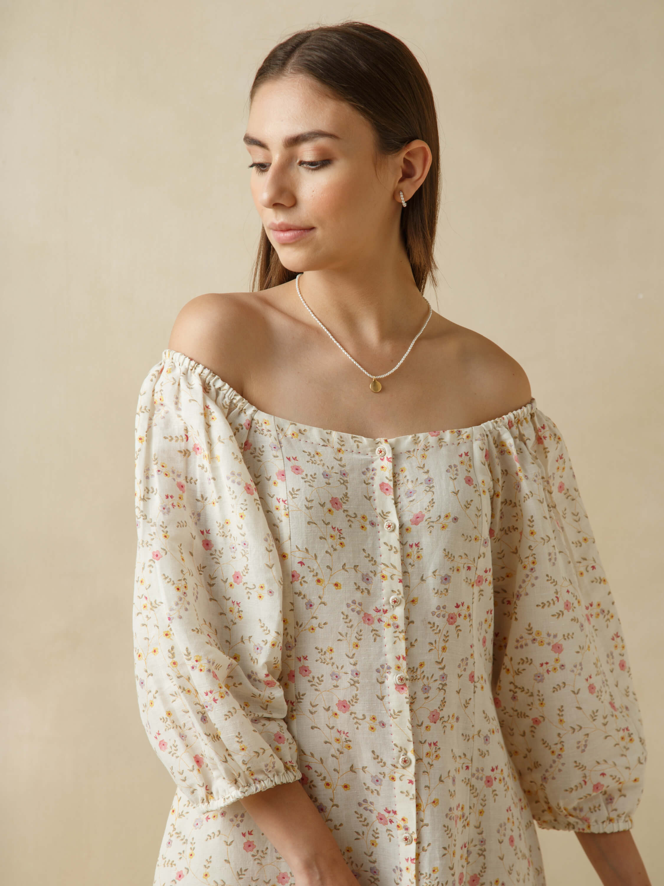 Woman wearing a floral off-shoulder dress with necklace and earrings.