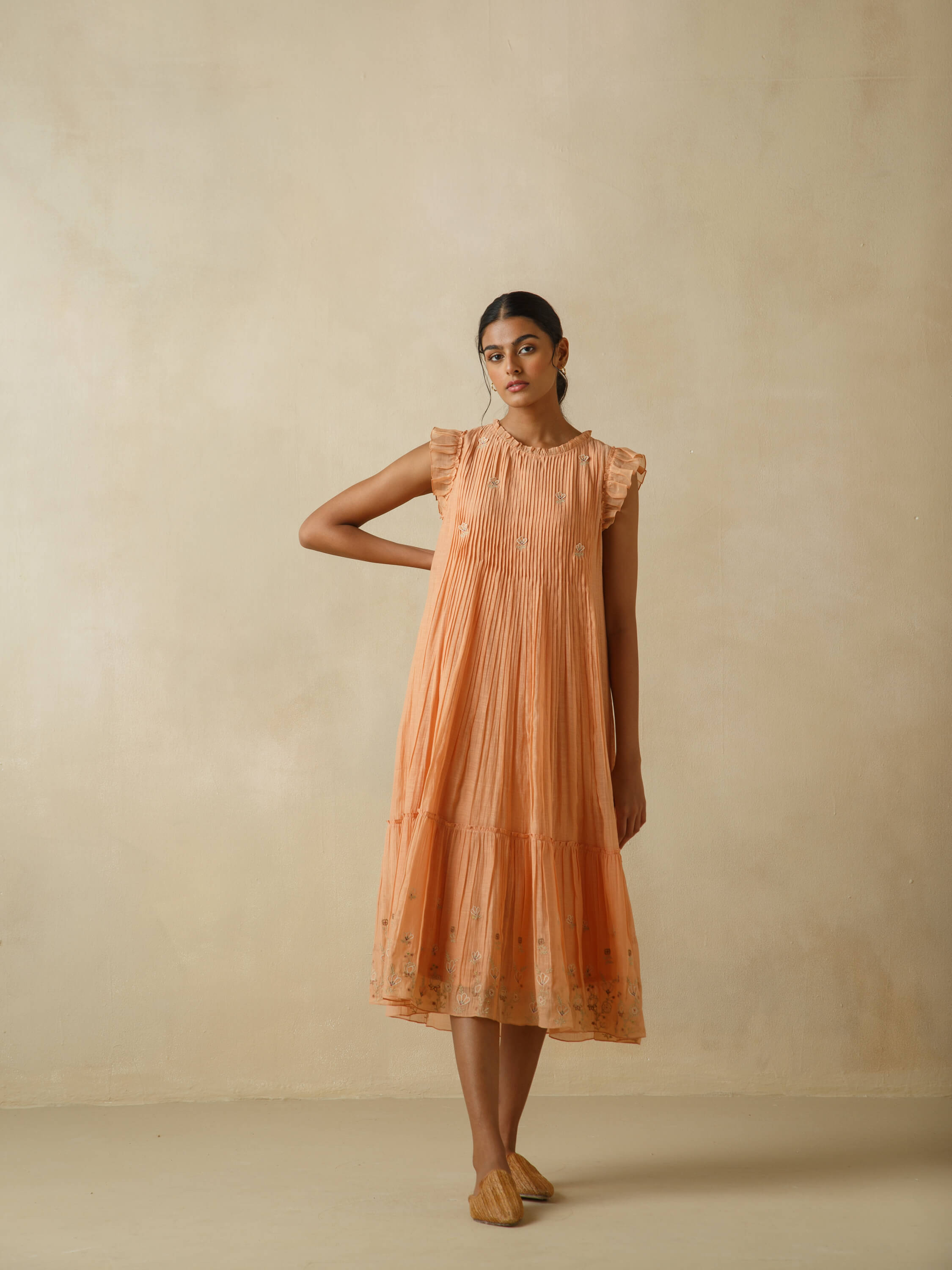Woman wearing peach floral dress with pleated detailing.