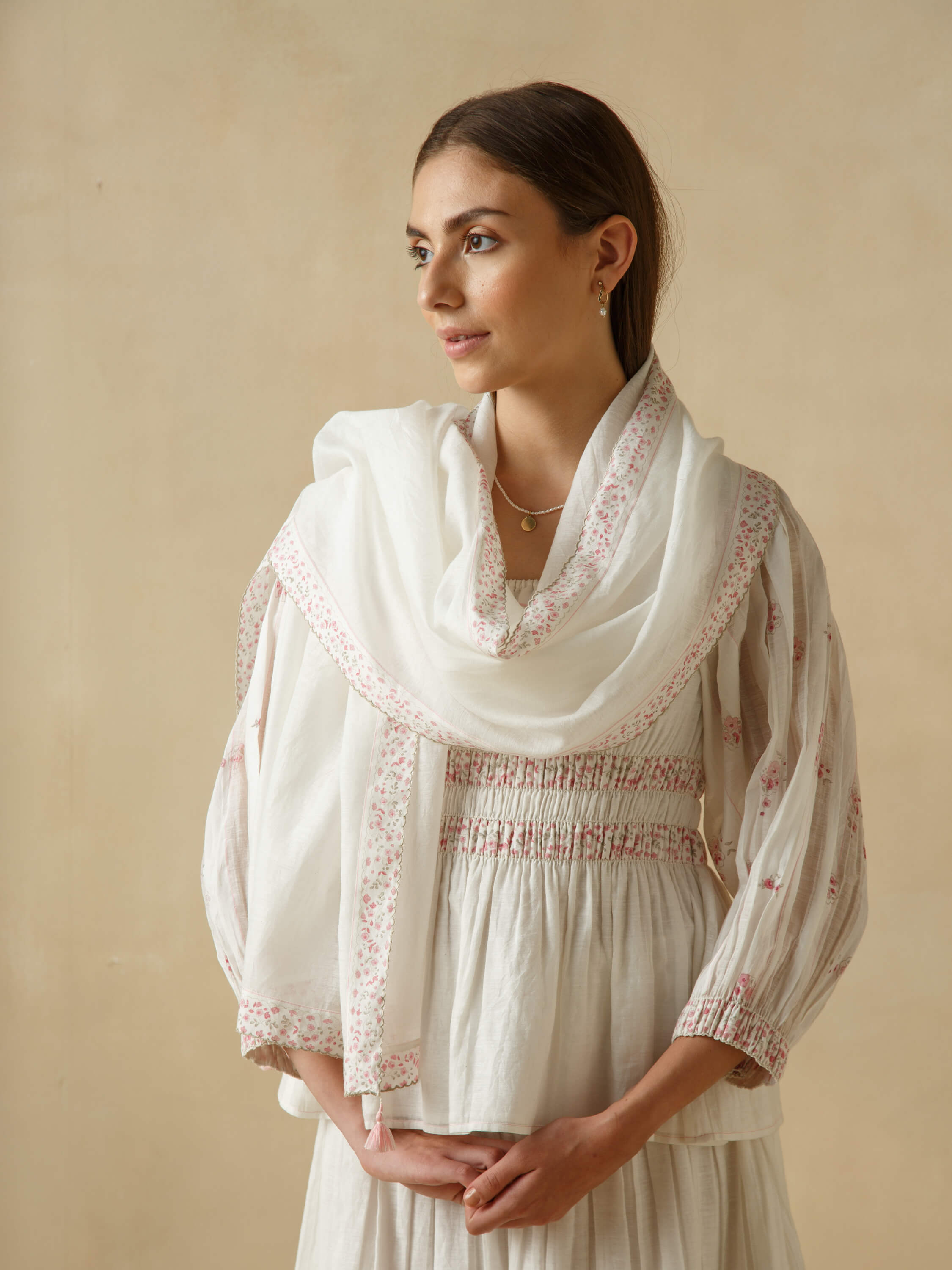 Woman wearing traditional white dress with floral embroidery, gazing to the side.
