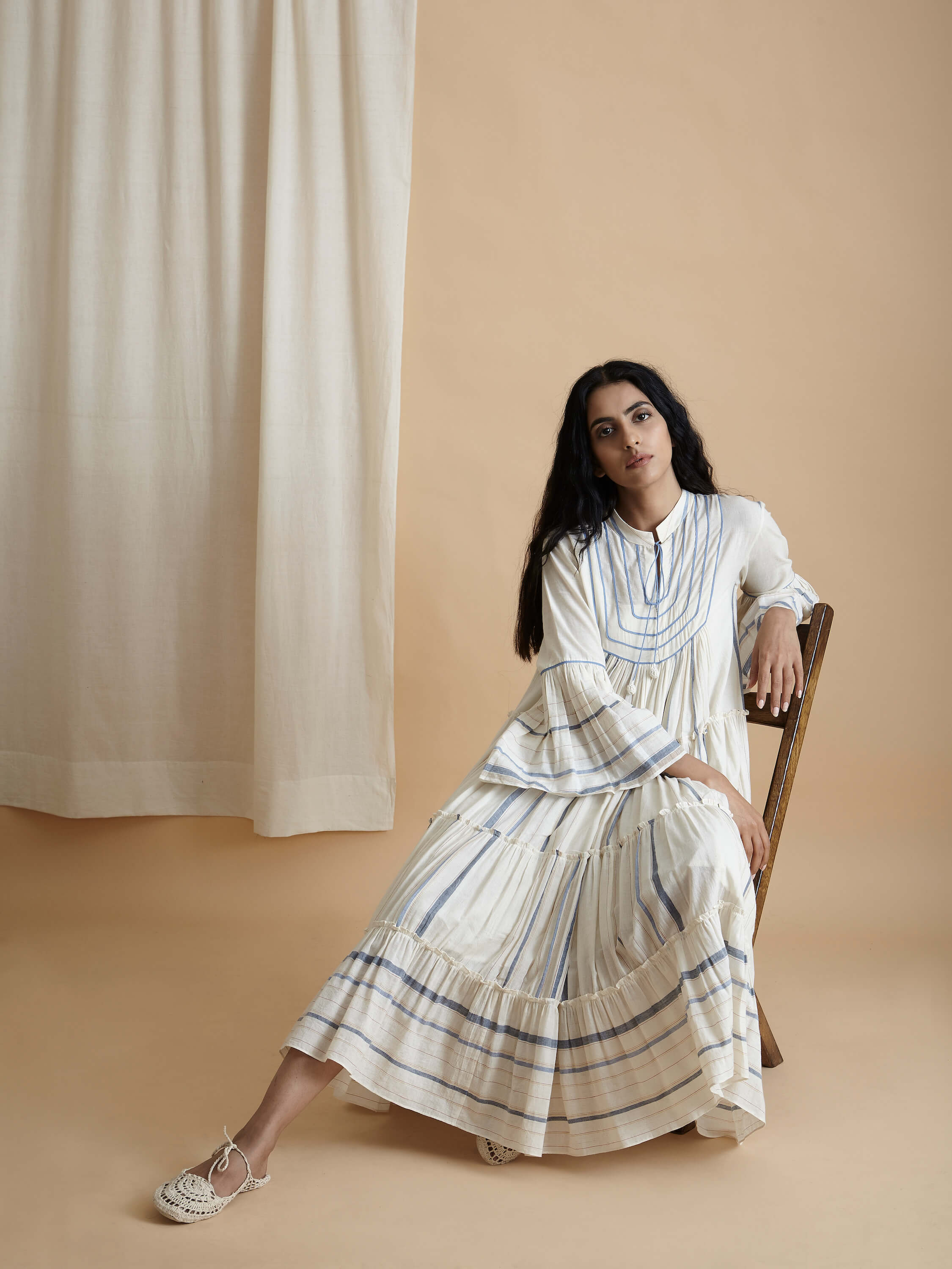 Woman in flowing white dress sitting against beige backdrop.