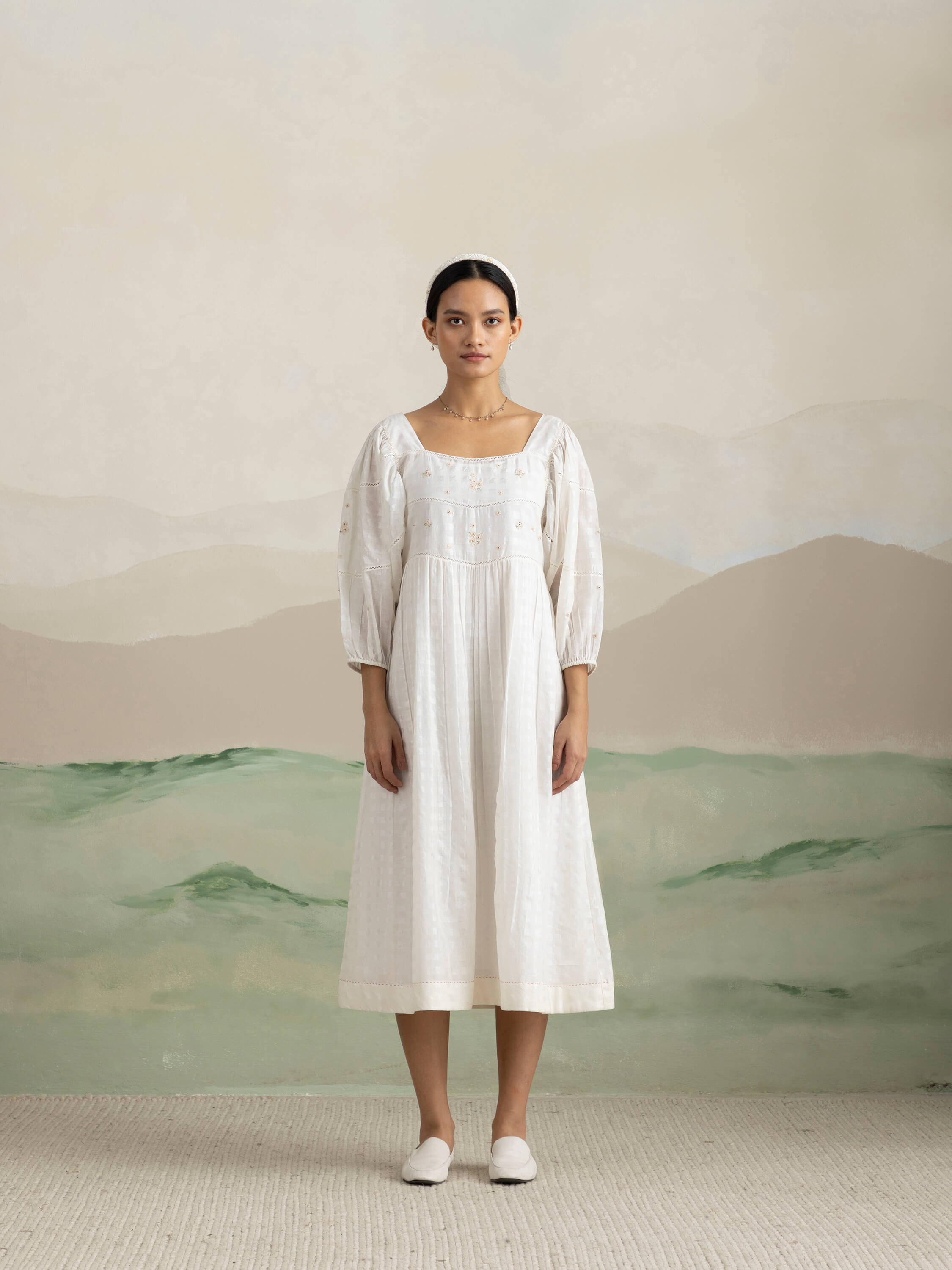 Woman wearing a white dress standing against a serene, minimalist background.