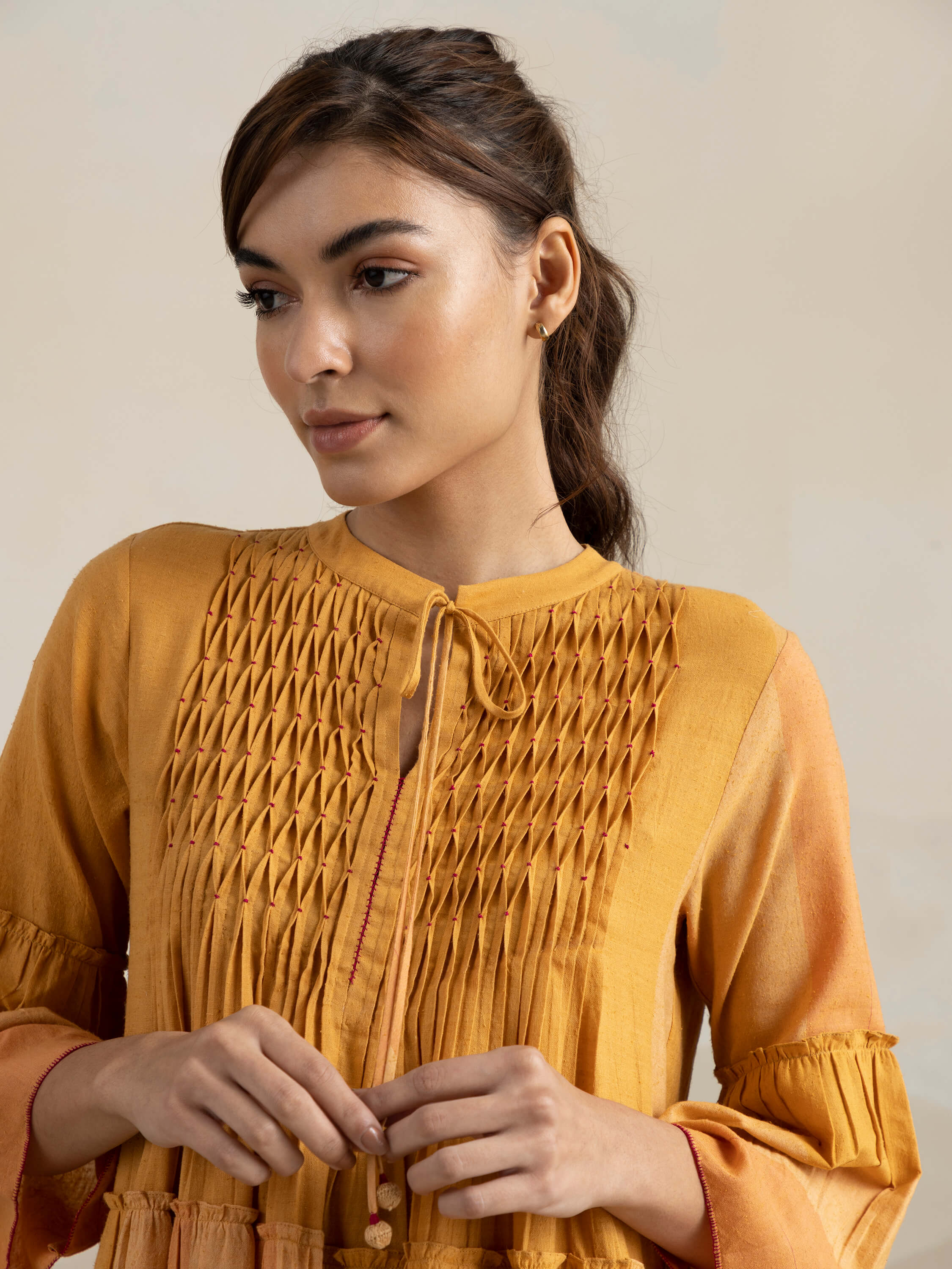 Woman wearing a mustard yellow embroidered top, hair tied back.
