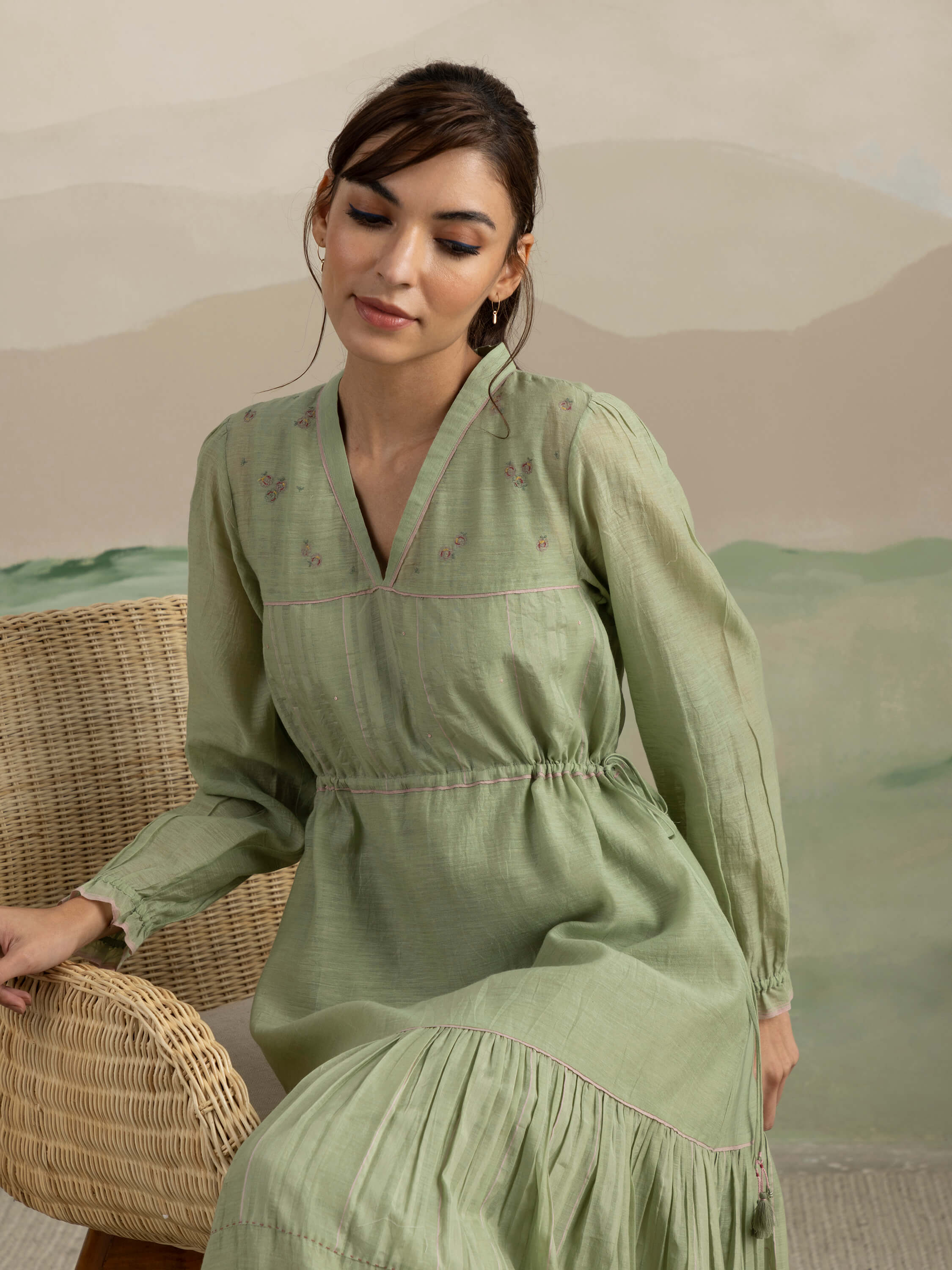 Woman in green dress sitting on wicker chair, serene background.