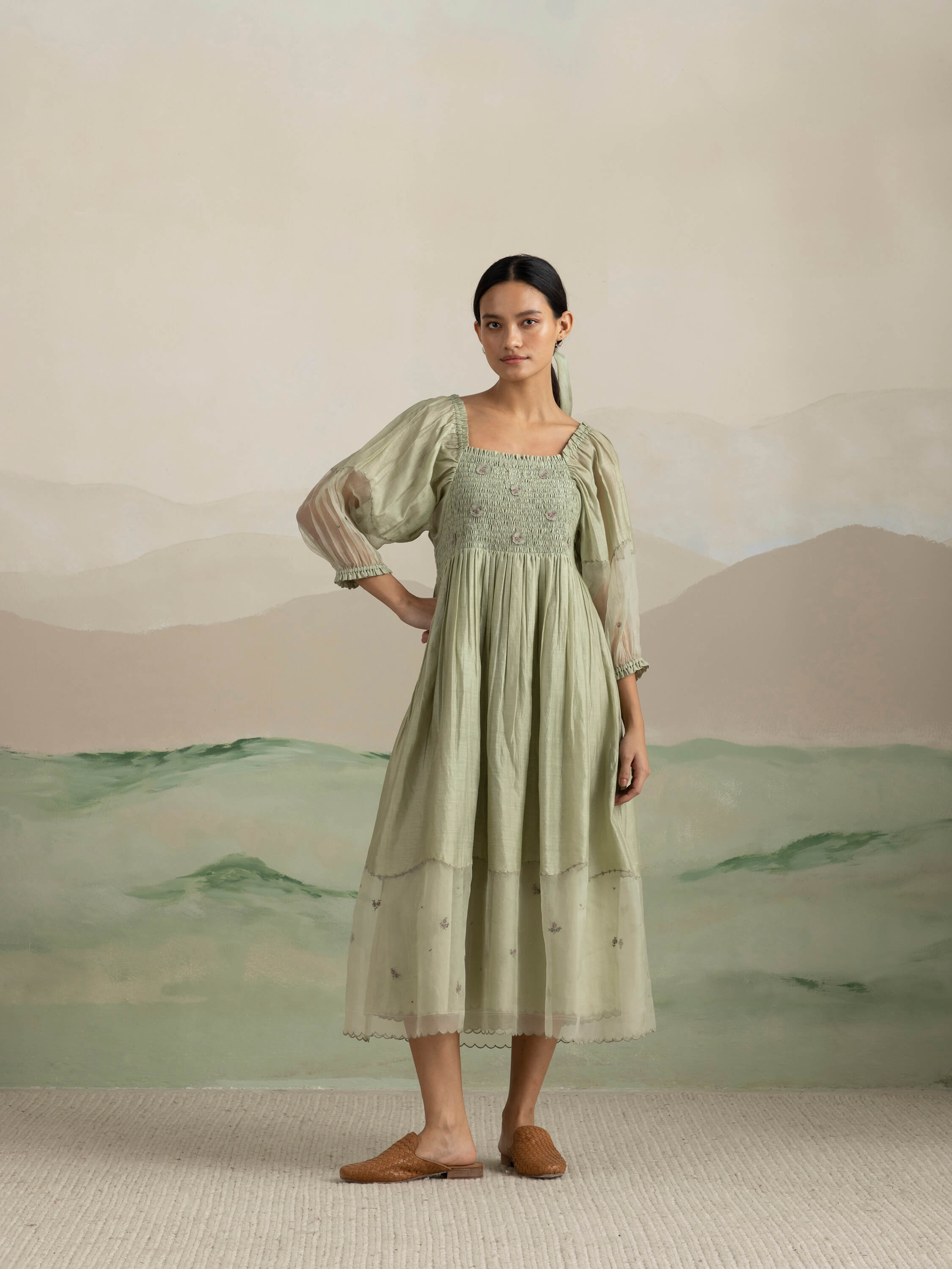 Woman wearing a green dress standing in front of a scenic backdrop.