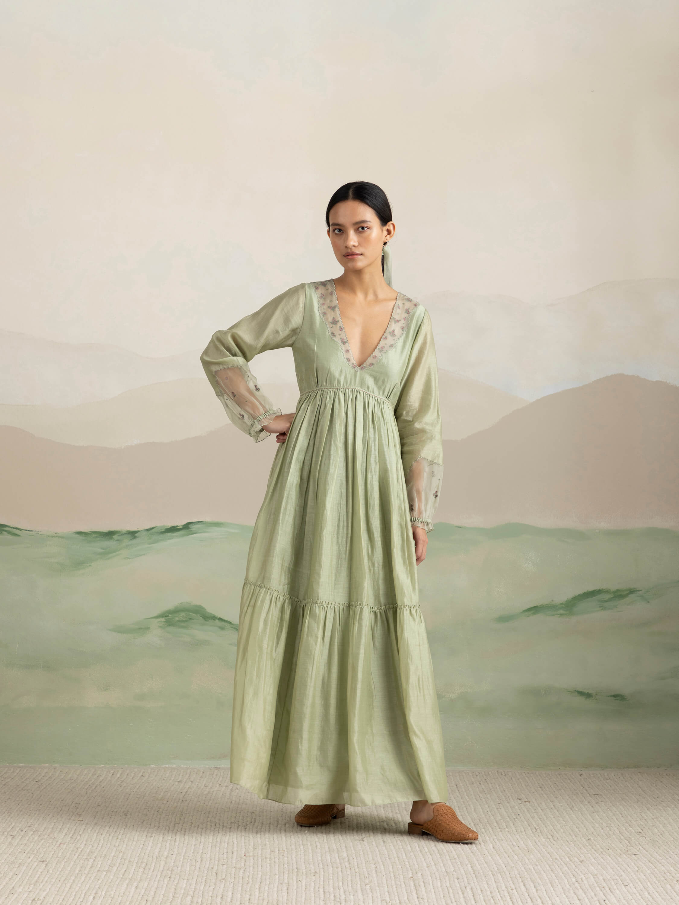 Woman in light green long dress posing in front of abstract background.