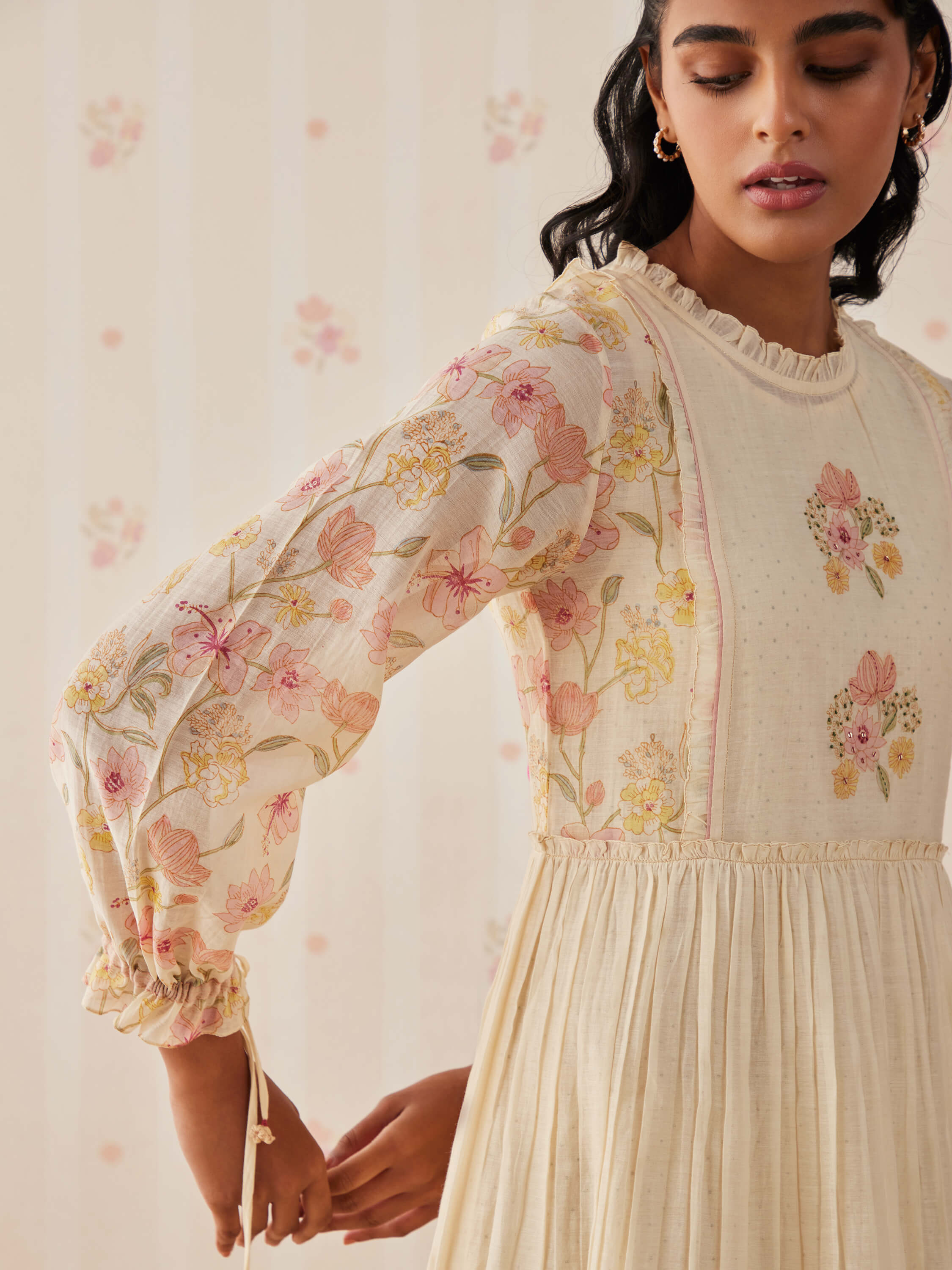 Woman wearing floral embroidered long-sleeve cream dress with ruffled neckline.