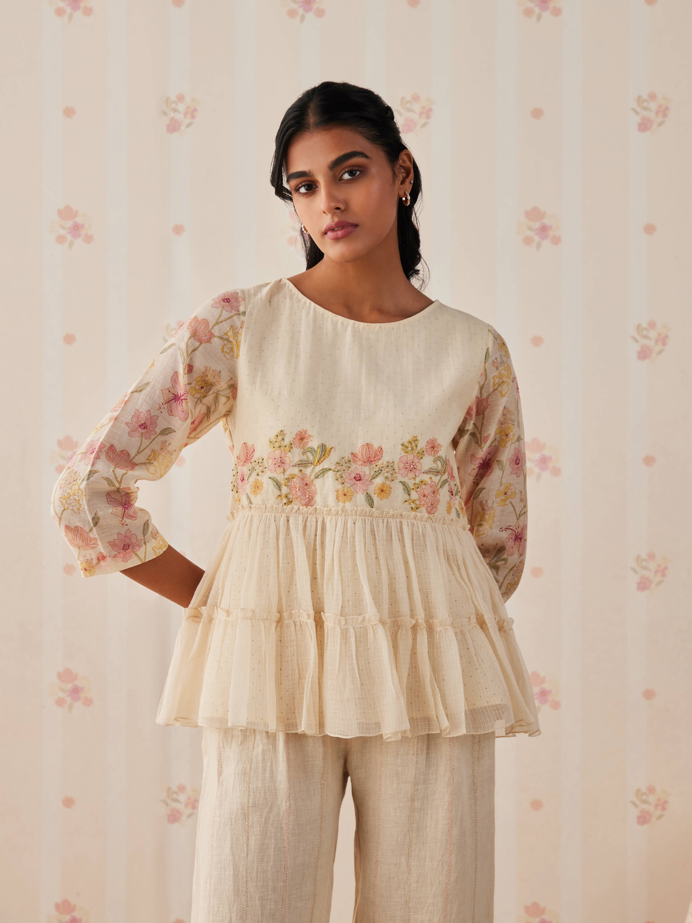 Woman wearing a floral embroidered cream top with tiered ruffles.