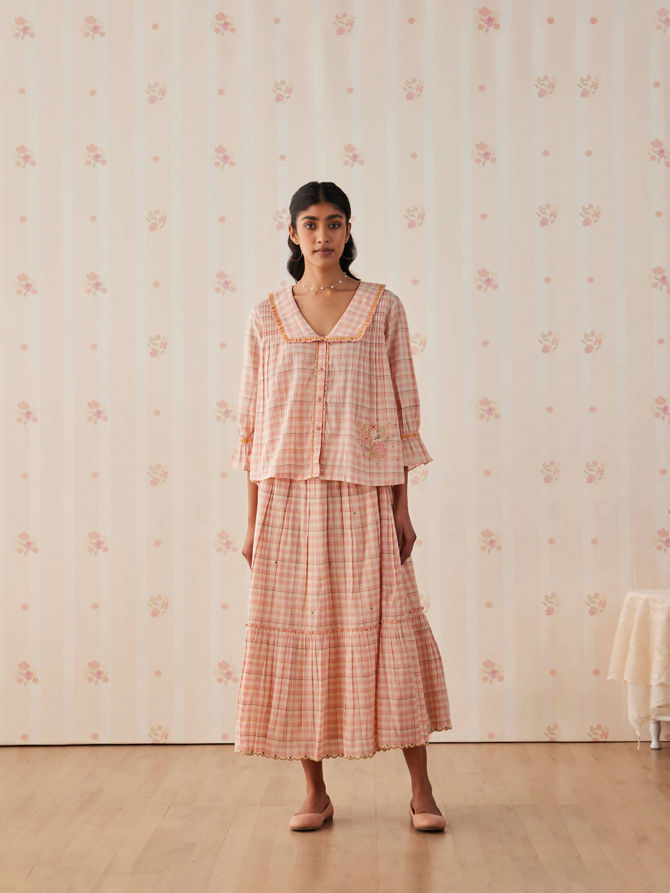 Woman in pink plaid dress with floral wallpaper background.