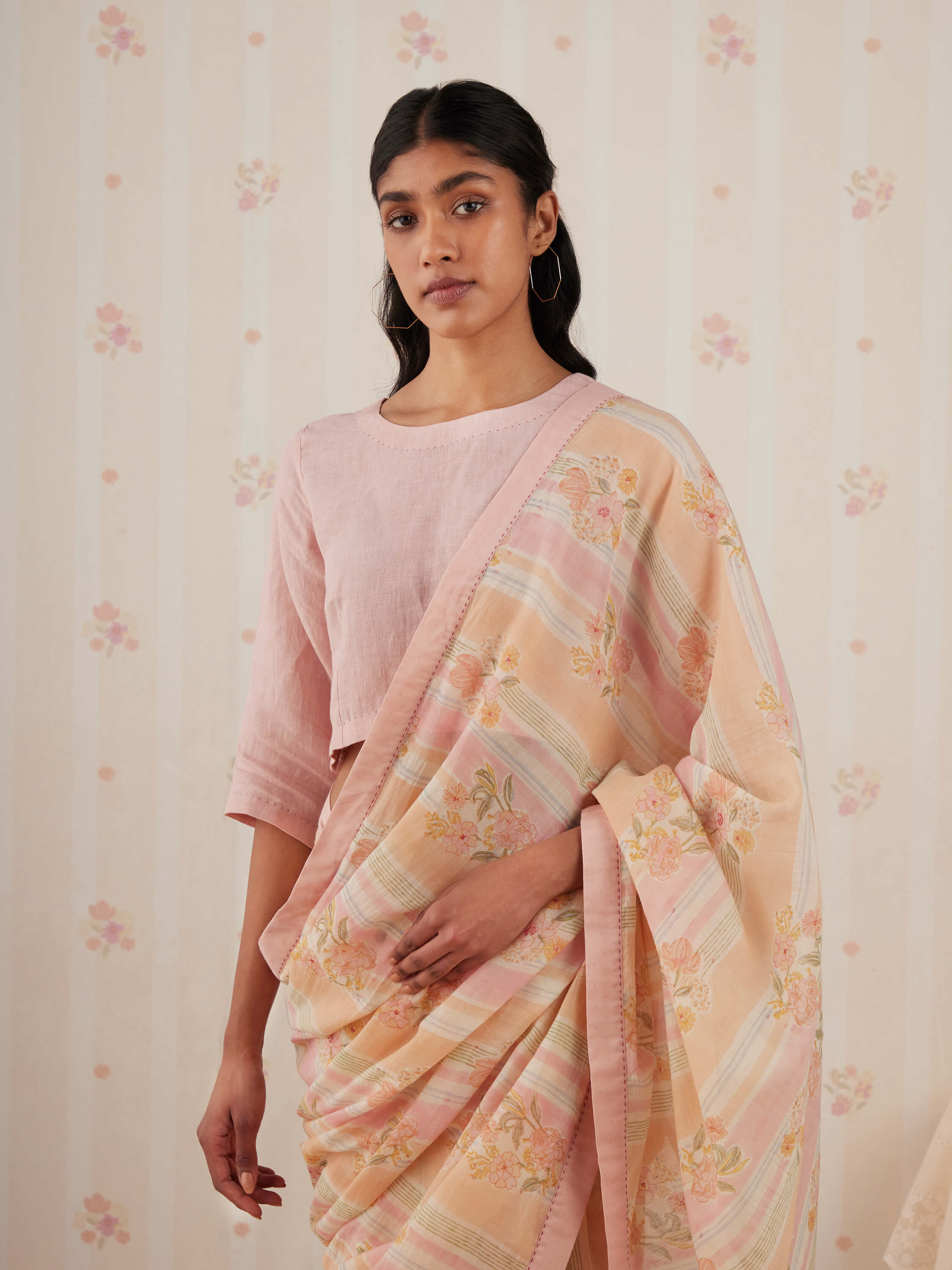 Woman in pastel pink and peach floral saree, elegant traditional attire.