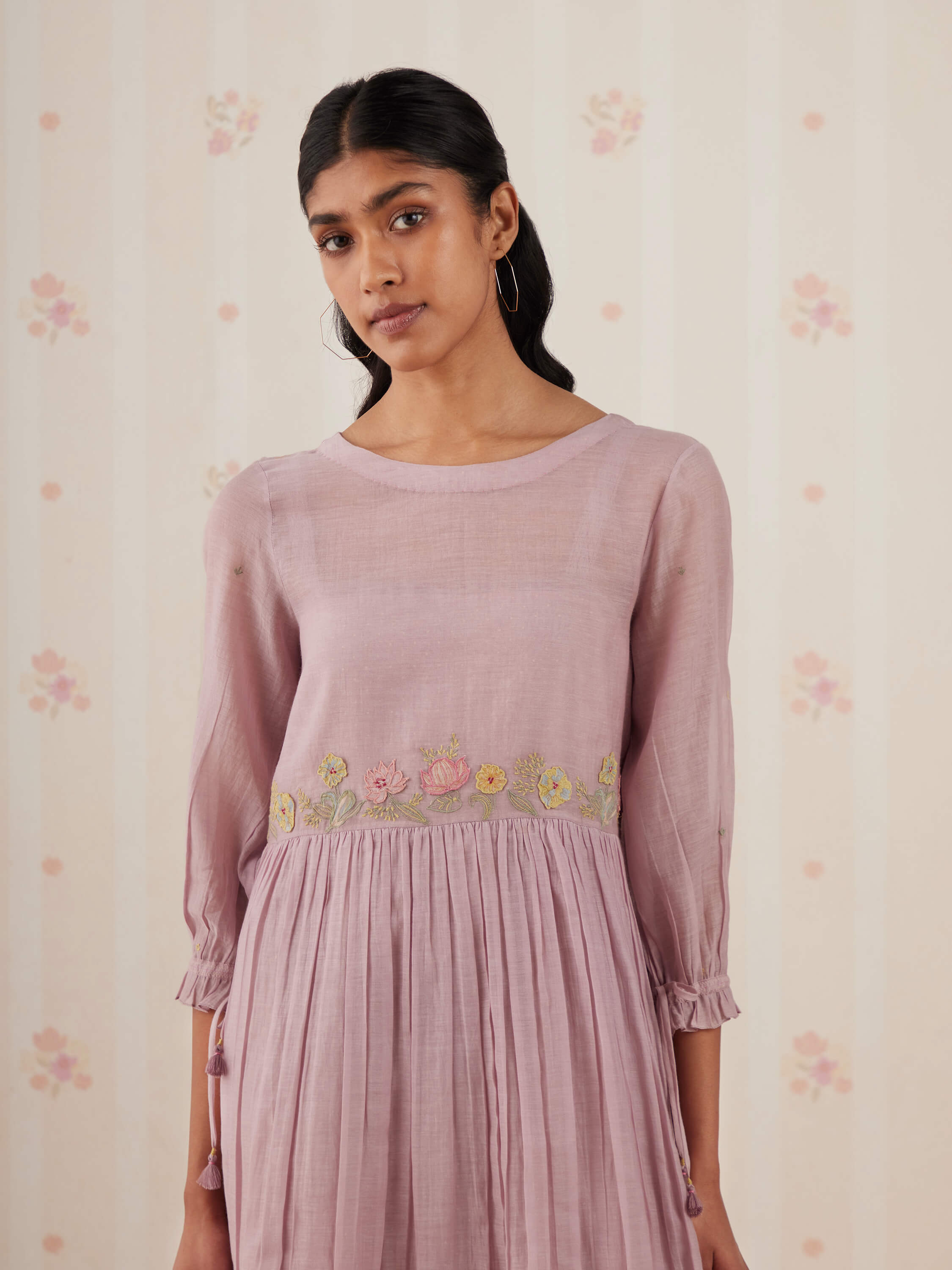 Woman wearing a pink embroidered dress with floral pattern.