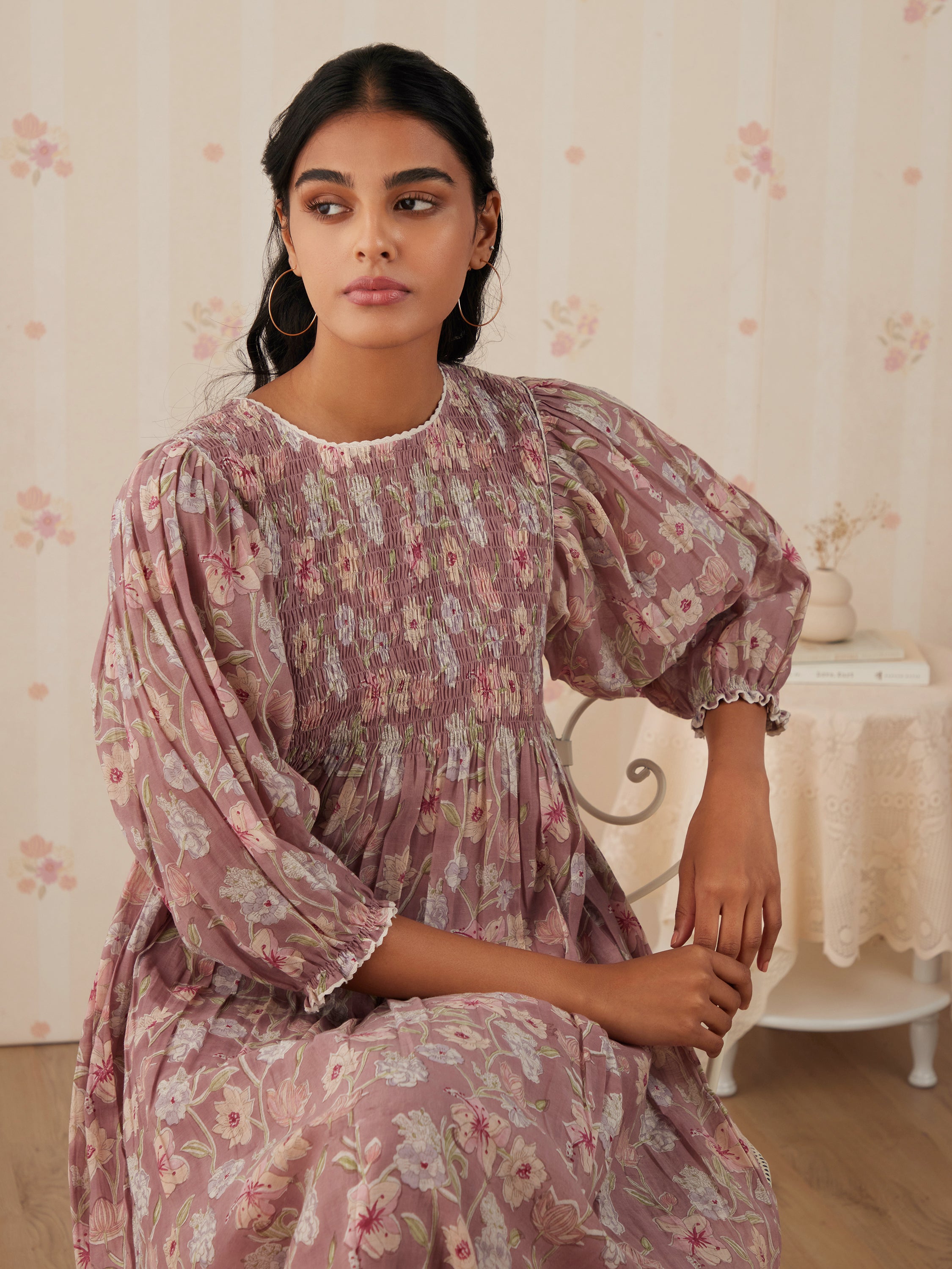 Young woman in floral dress sitting in vintage-style room.