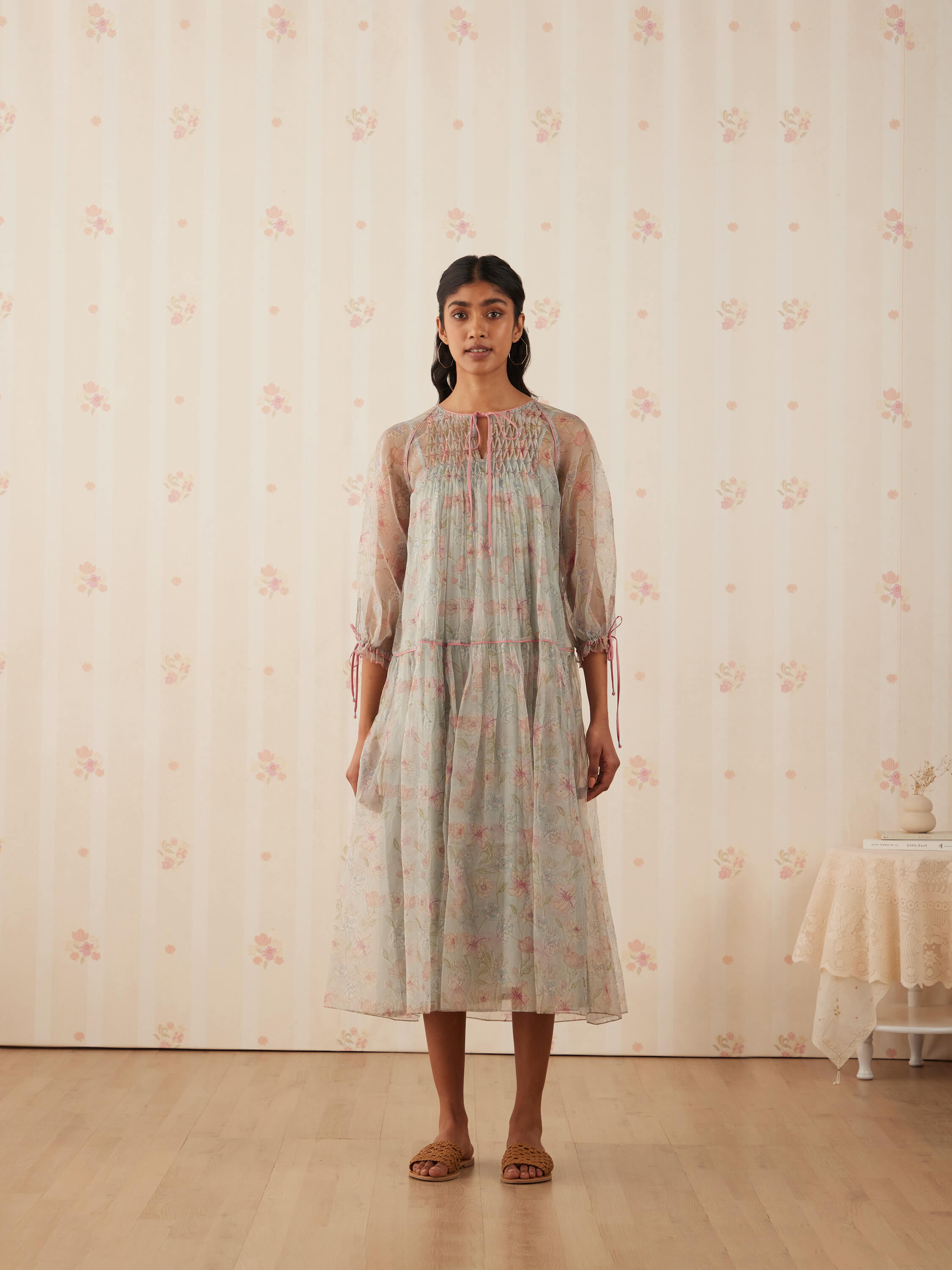 Woman wearing a floral dress stands in a vintage-themed room.